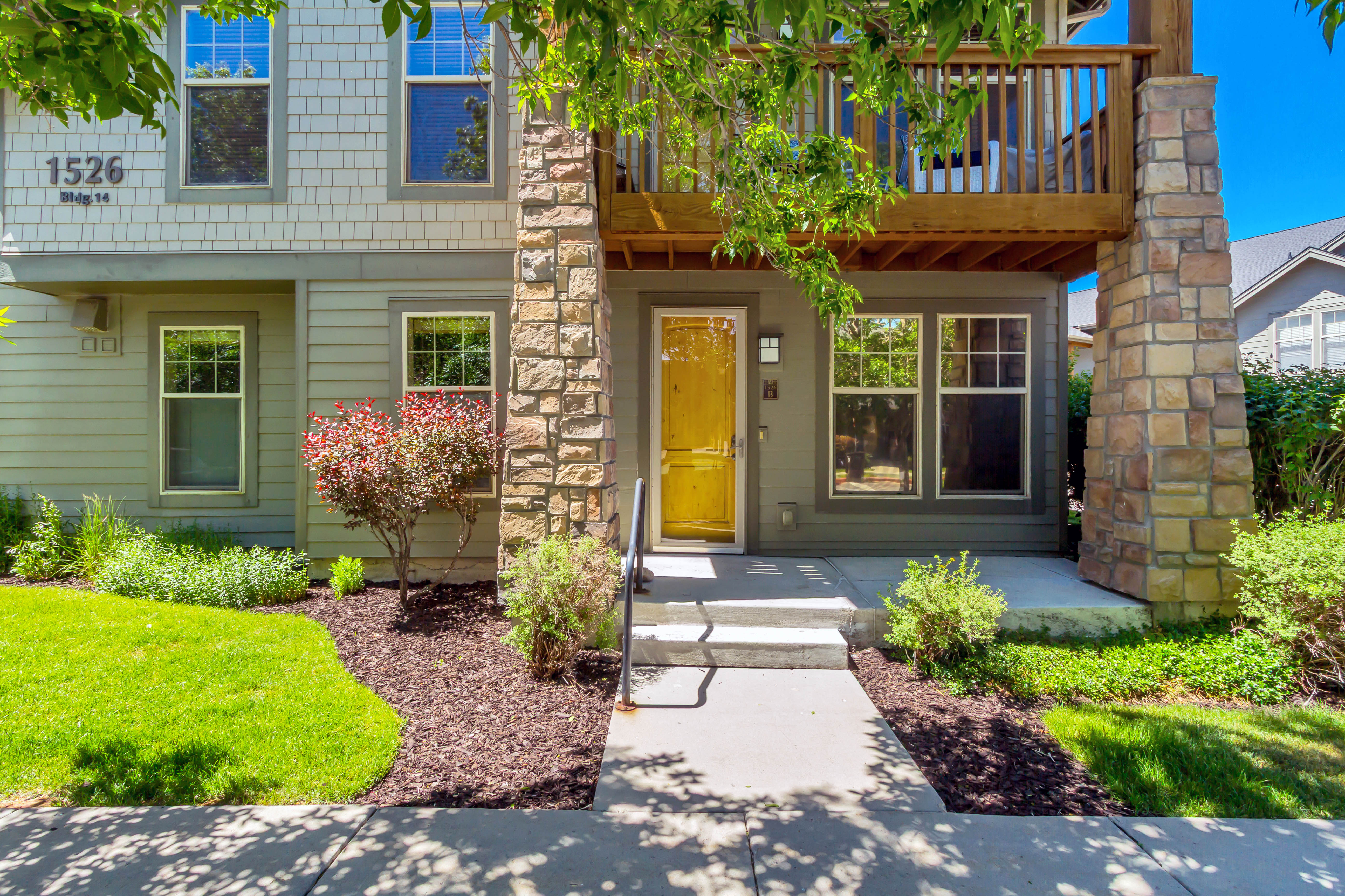 Contemporary exterior featuring a yellow entry door, stone pillar accents, and a second-story balcony