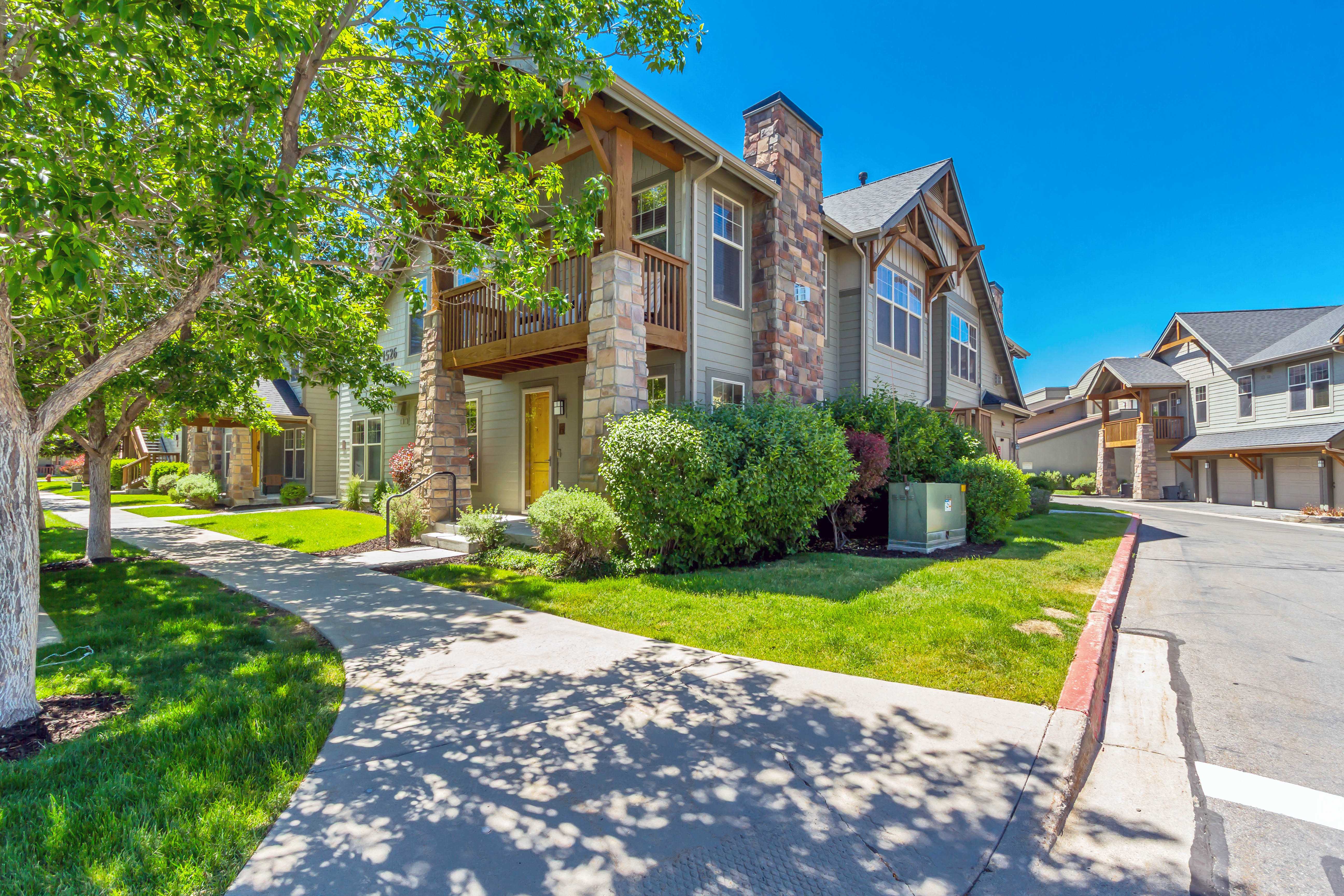 Townhome exterior featuring stone accents, wood beam detailing, a second-story balcony, and a prominent yellow entry door