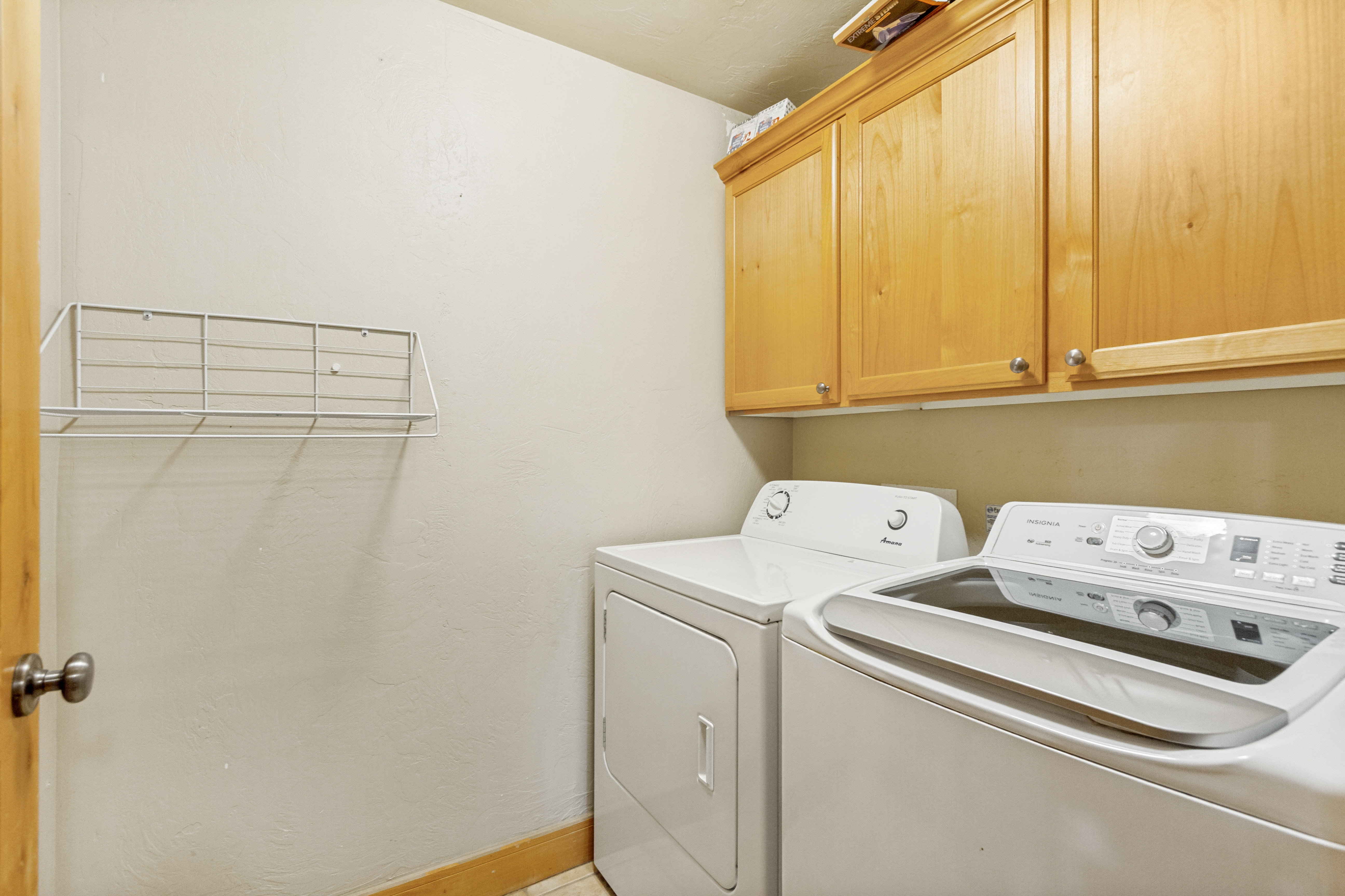Laundry area featuring light wood-finish cabinetry with silver-tone hardware, a wall-mounted drying rack, and wood-finish trim