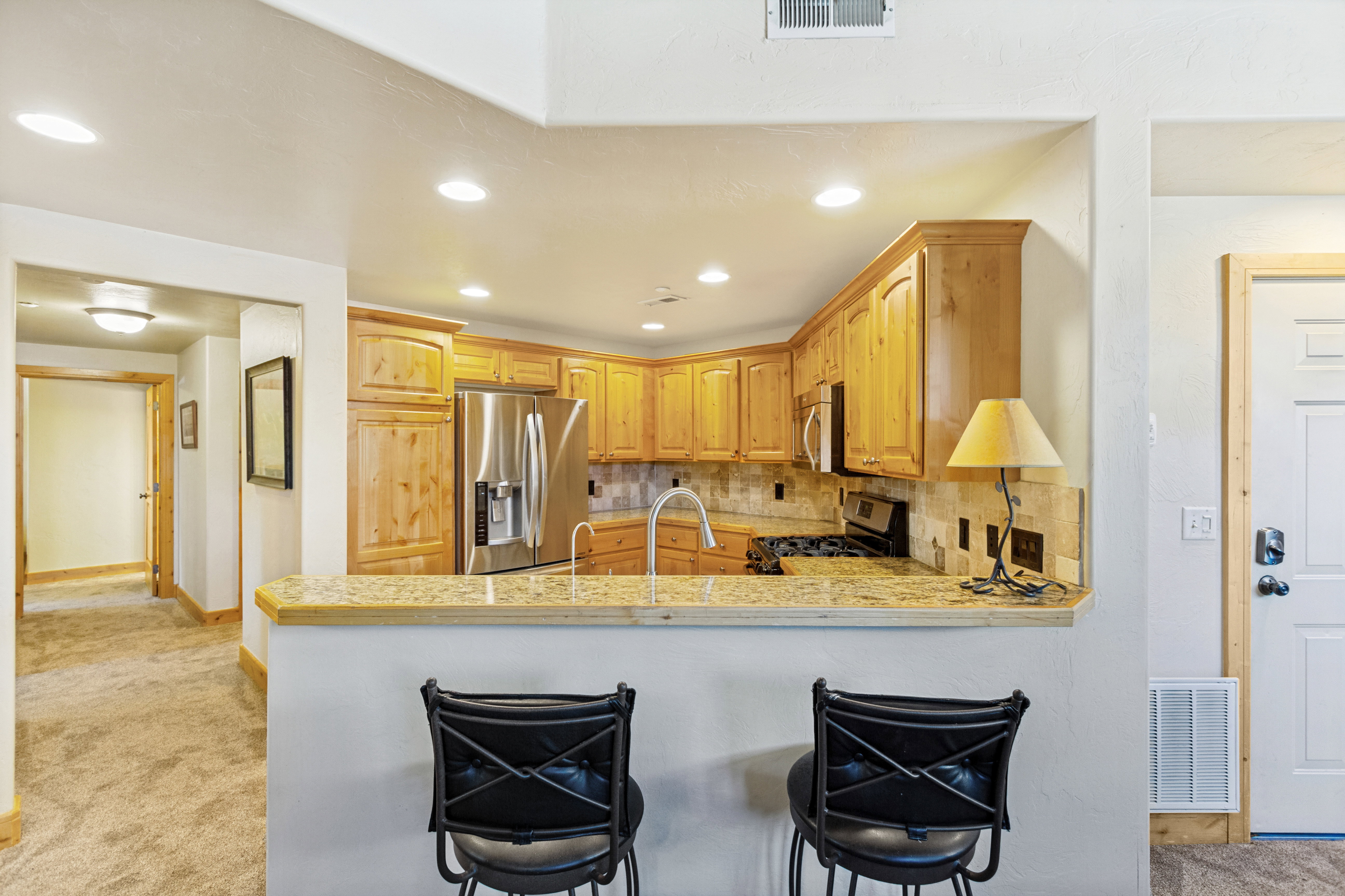 Kitchen featuring wood-finish cabinetry, stainless steel appliances, and a stone-finish countertop with a matching backsplash