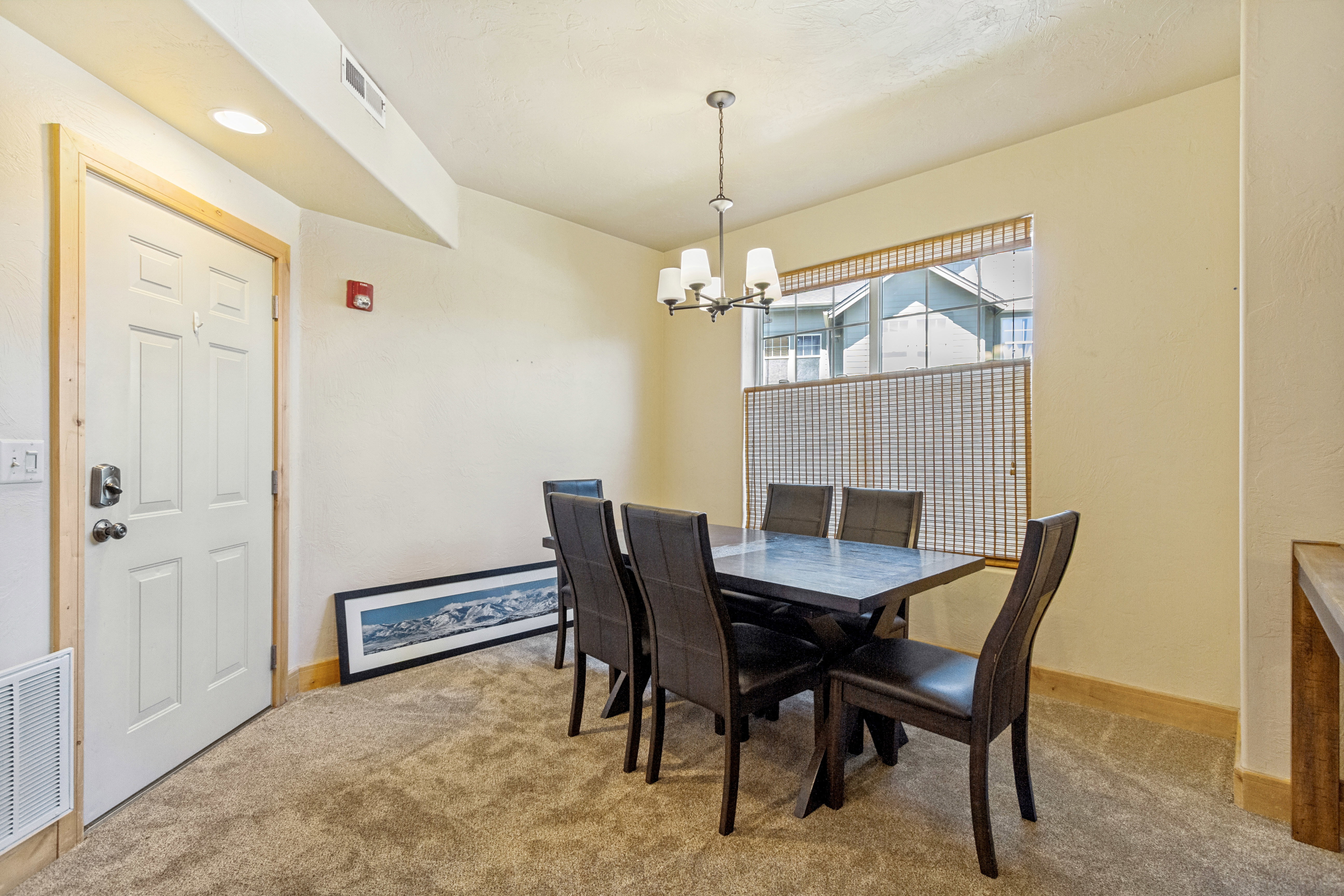 Dining area featuring a contemporary chandelier, textured carpet flooring, and a large window with woven blinds