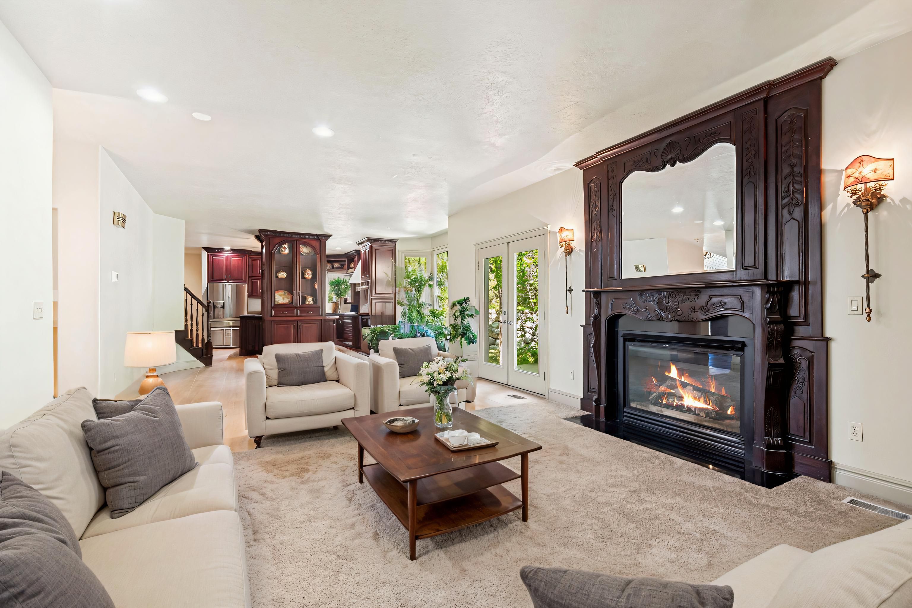 Spacious living area featuring a large ornate dark wood fireplace with an integrated mirror, recessed ceiling lighting, and light-colored carpet flooring