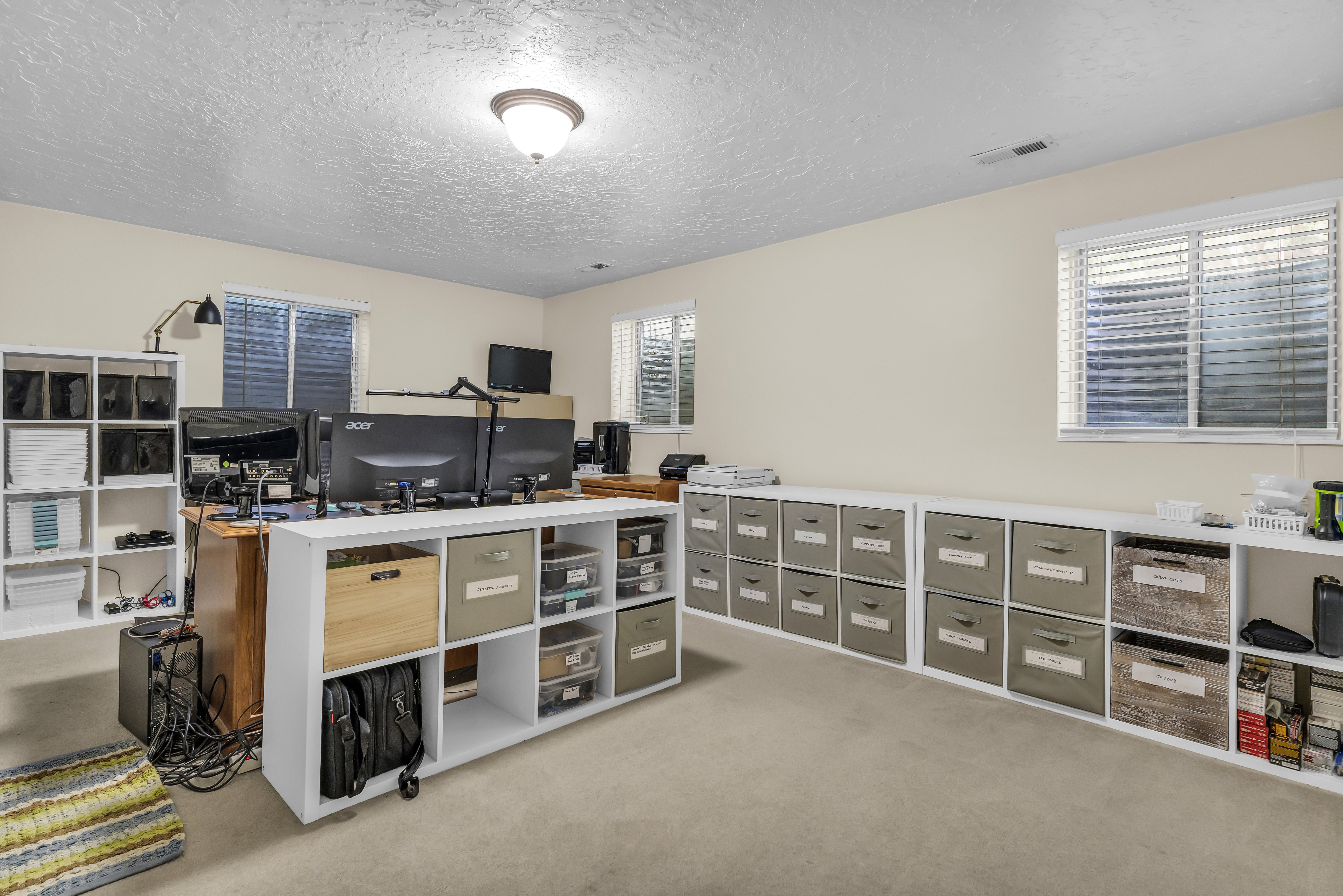 Spacious room featuring neutral carpeting, multiple windows with horizontal blinds, and a built-in shelving unit providing extensive storage