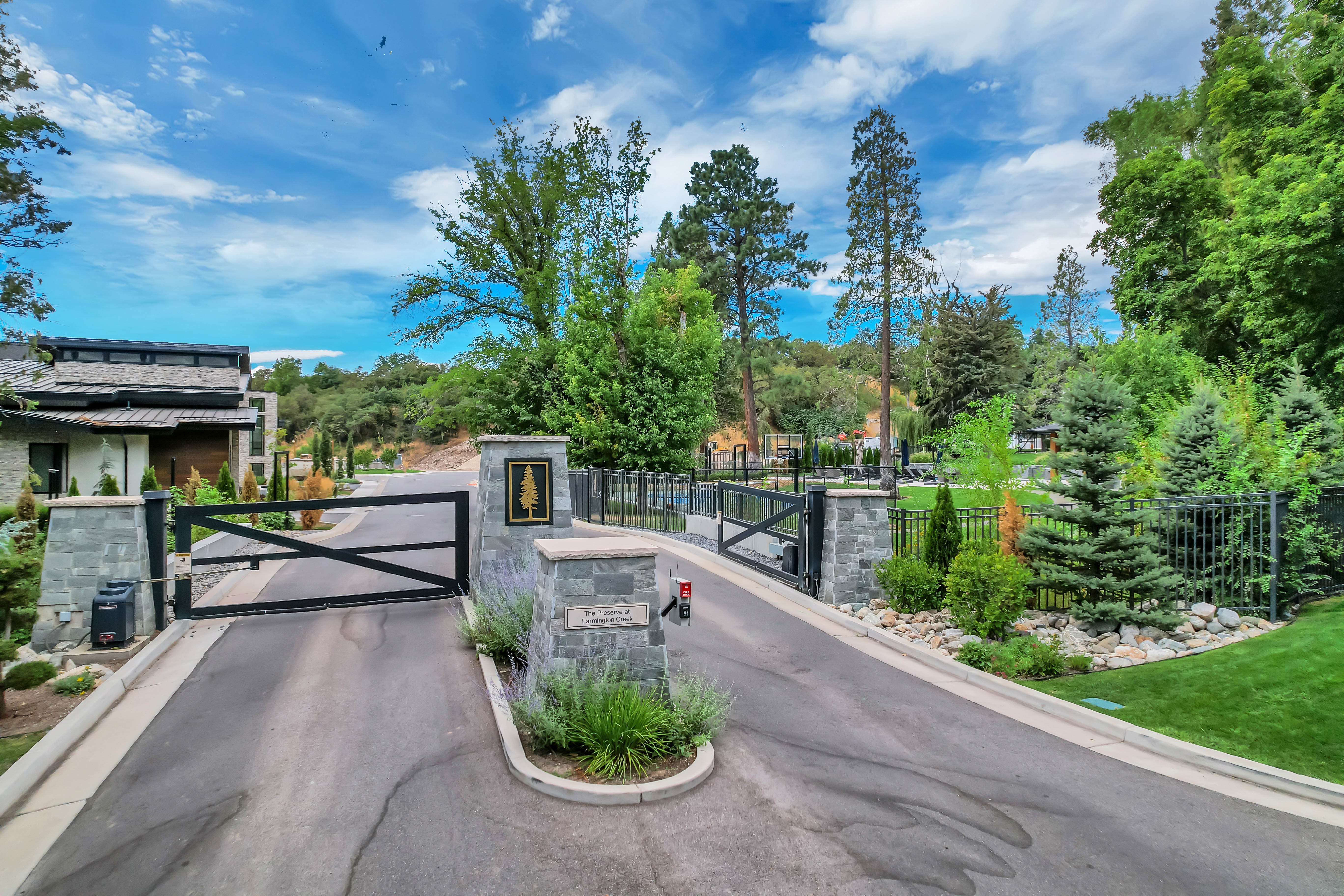 Gated entrance featuring stone pillars, black metal gates, and lush surrounding landscaping