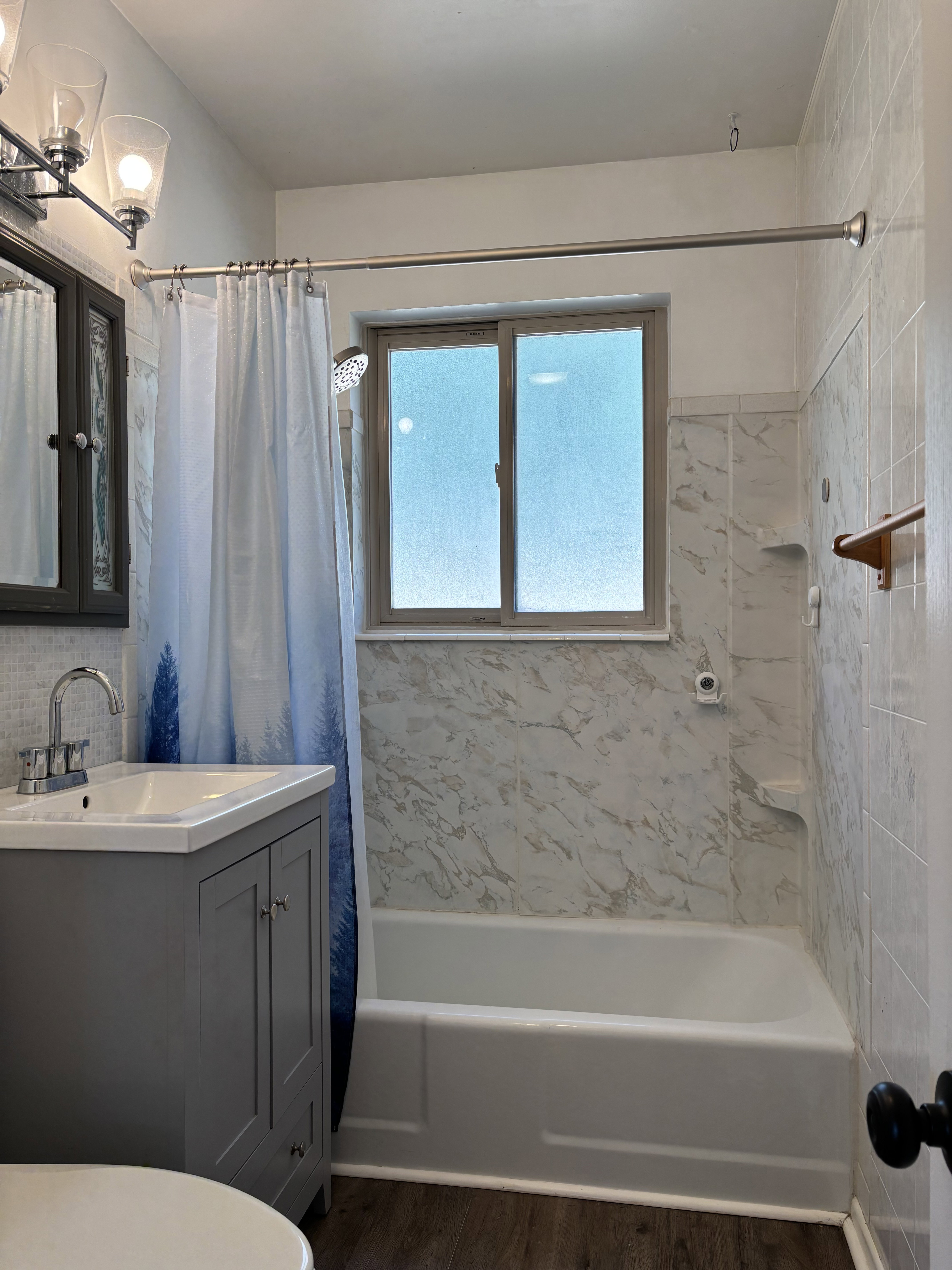 Bathroom featuring a single vanity with a white countertop and gray cabinetry, a white bathtub, and patterned wall tile