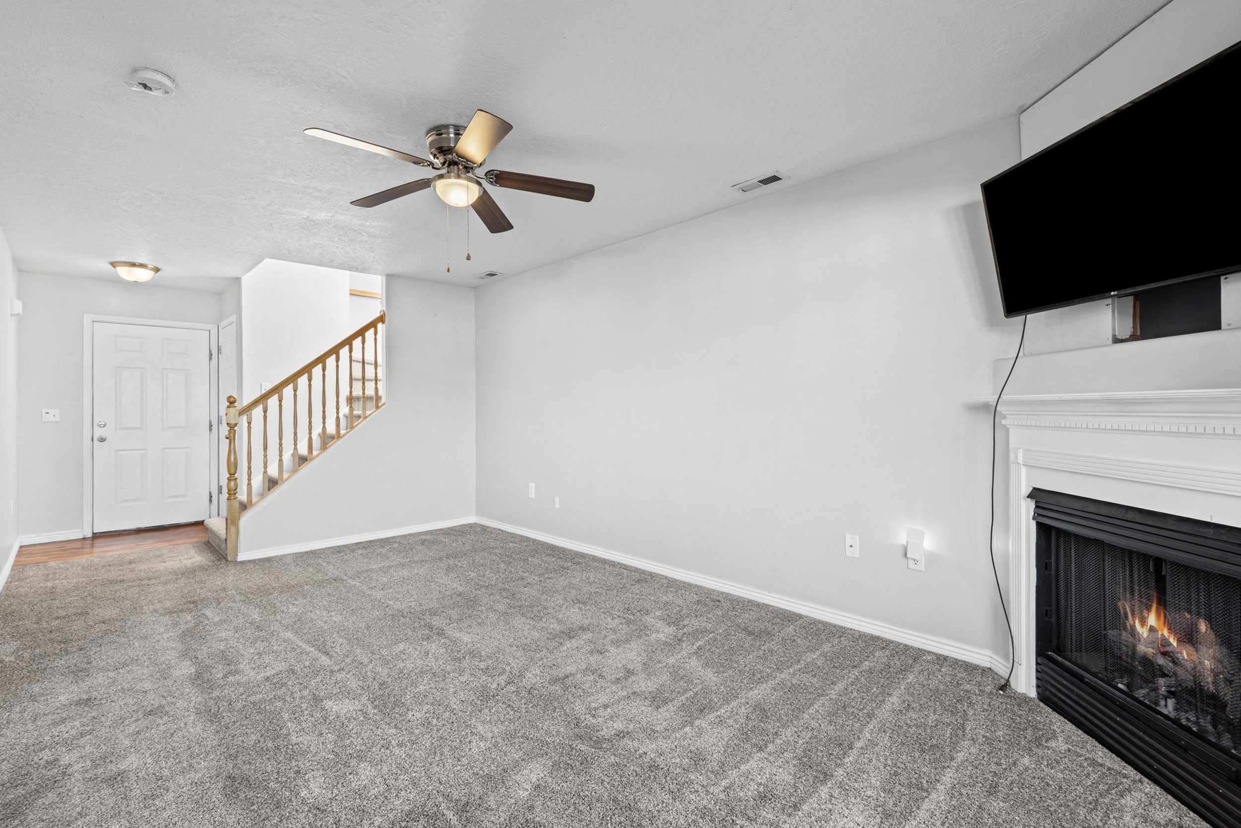 Living area featuring gray carpeting, a fireplace with a white mantel, and a ceiling fan with integrated lighting