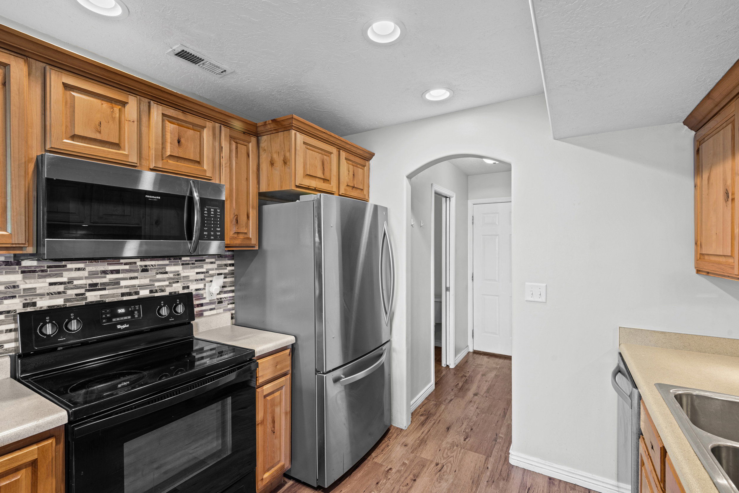 Kitchen featuring wood cabinetry, stainless steel appliances, mosaic tile backsplash, wood-finish flooring, and recessed lighting
