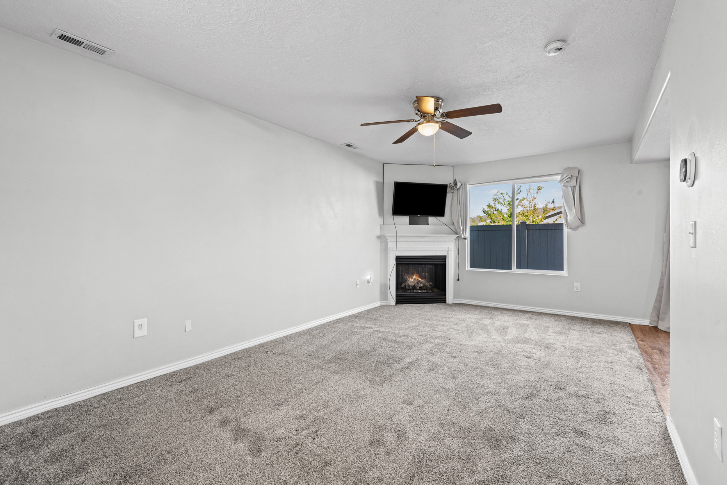 Living area featuring neutral-toned carpet, a corner fireplace with a white mantel, and a ceiling fan with integrated lighting