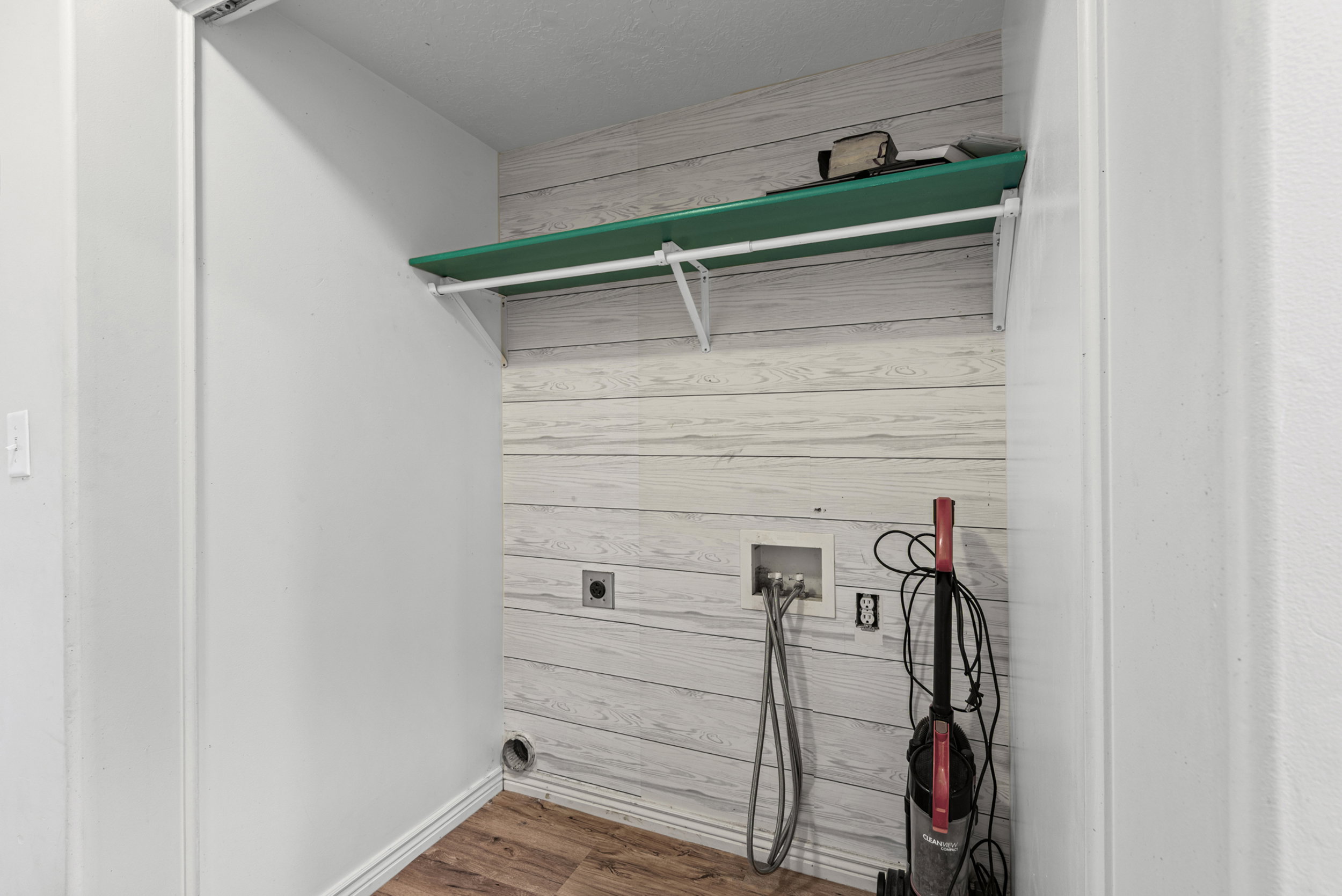 Utility closet featuring wood-finish flooring, shiplap-style wall paneling, and a mounted storage shelf