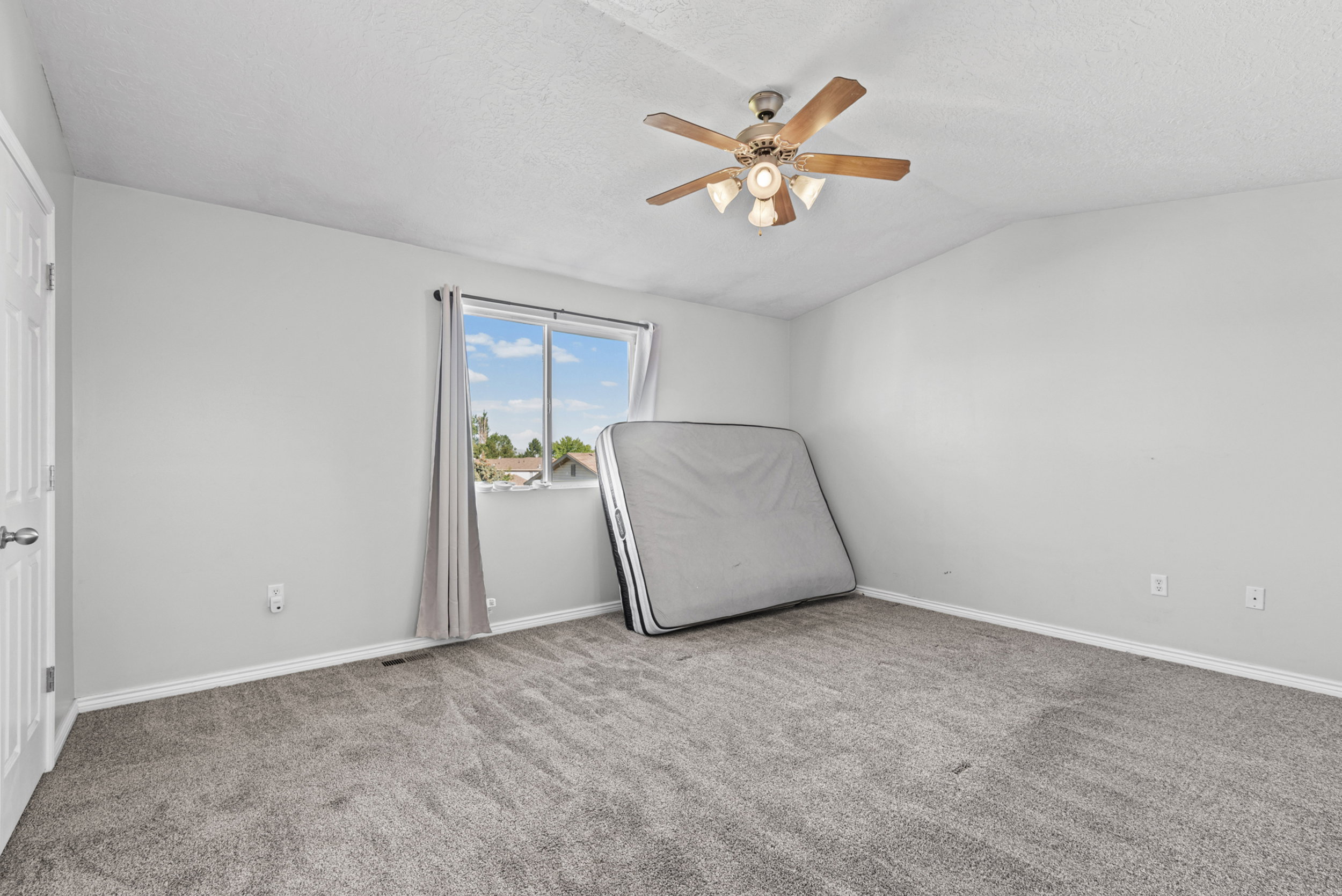 Carpeted room featuring a ceiling fan with integrated lighting, a window with curtains, and a paneled door