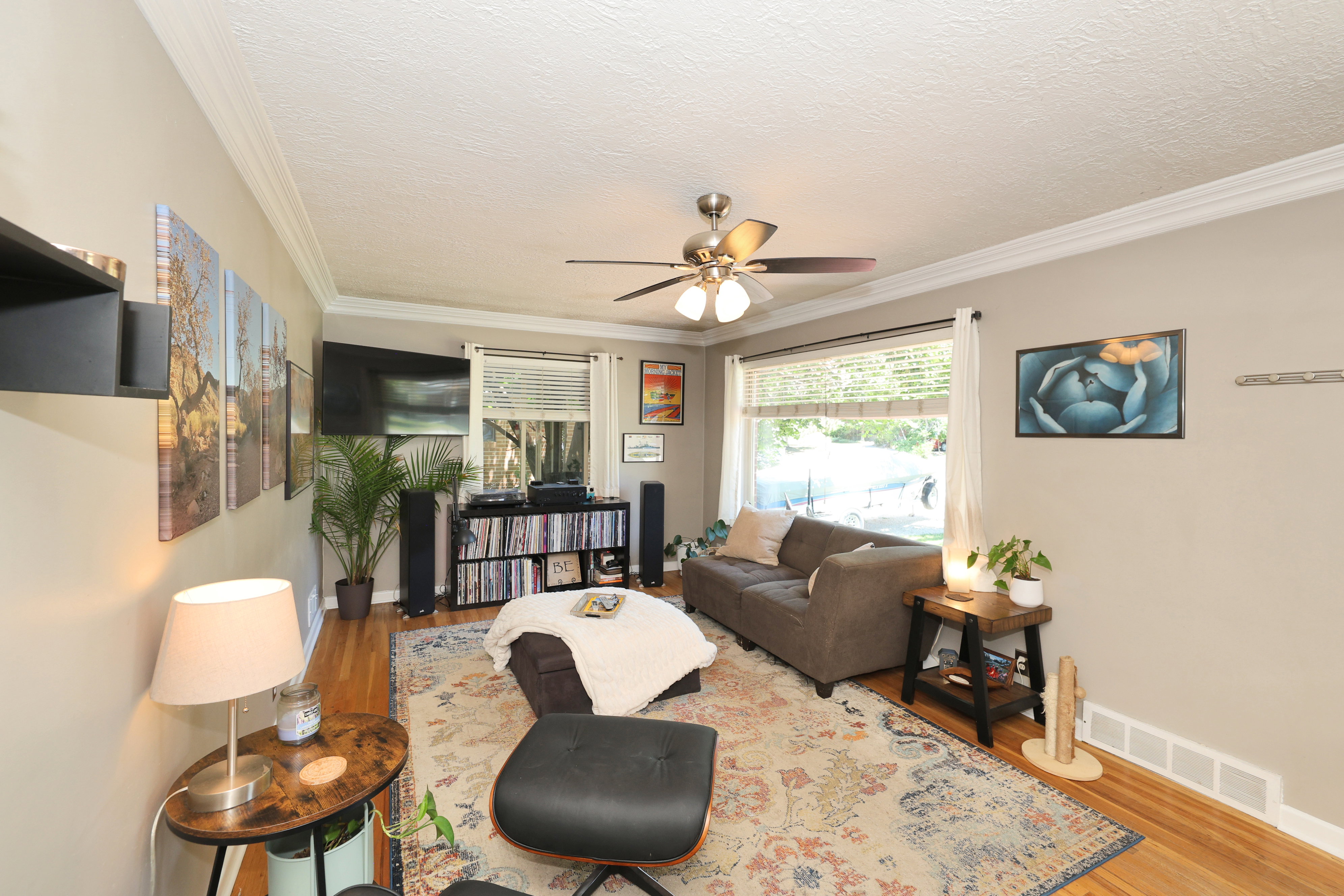 Living area featuring wood-finish flooring, crown molding, and a ceiling fan with integrated lighting
