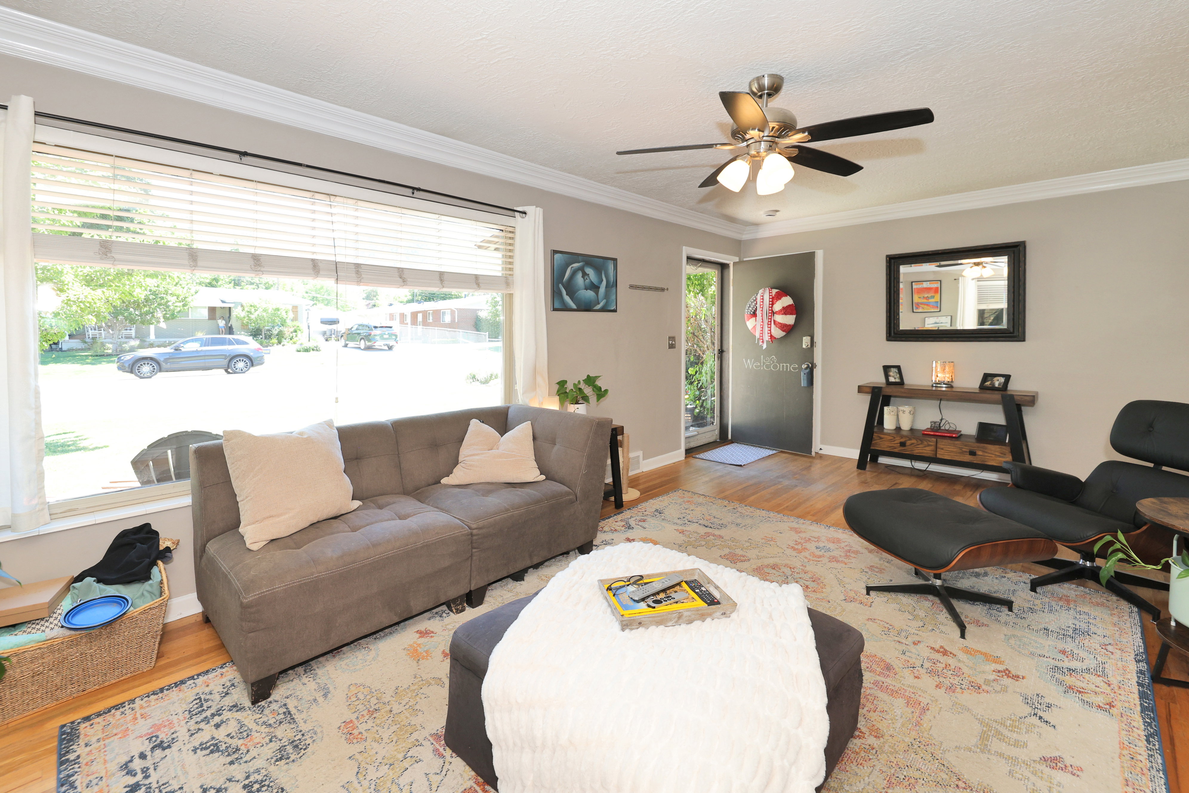 Living area featuring hardwood flooring, a large picture window with horizontal blinds, and a ceiling fan with integrated lighting