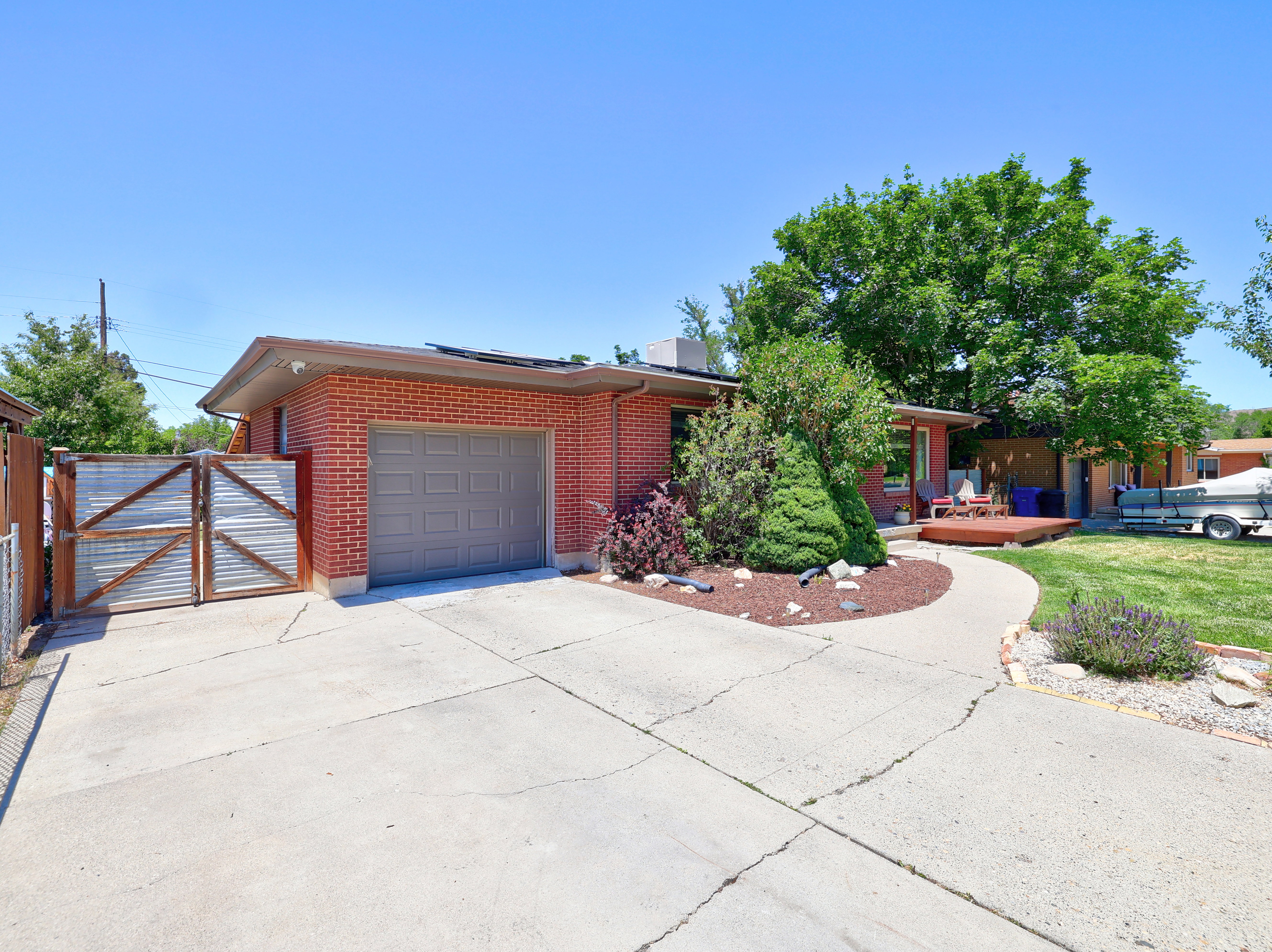 Brick exterior featuring an attached garage with a panel door, concrete driveway, and a separate gated paved area