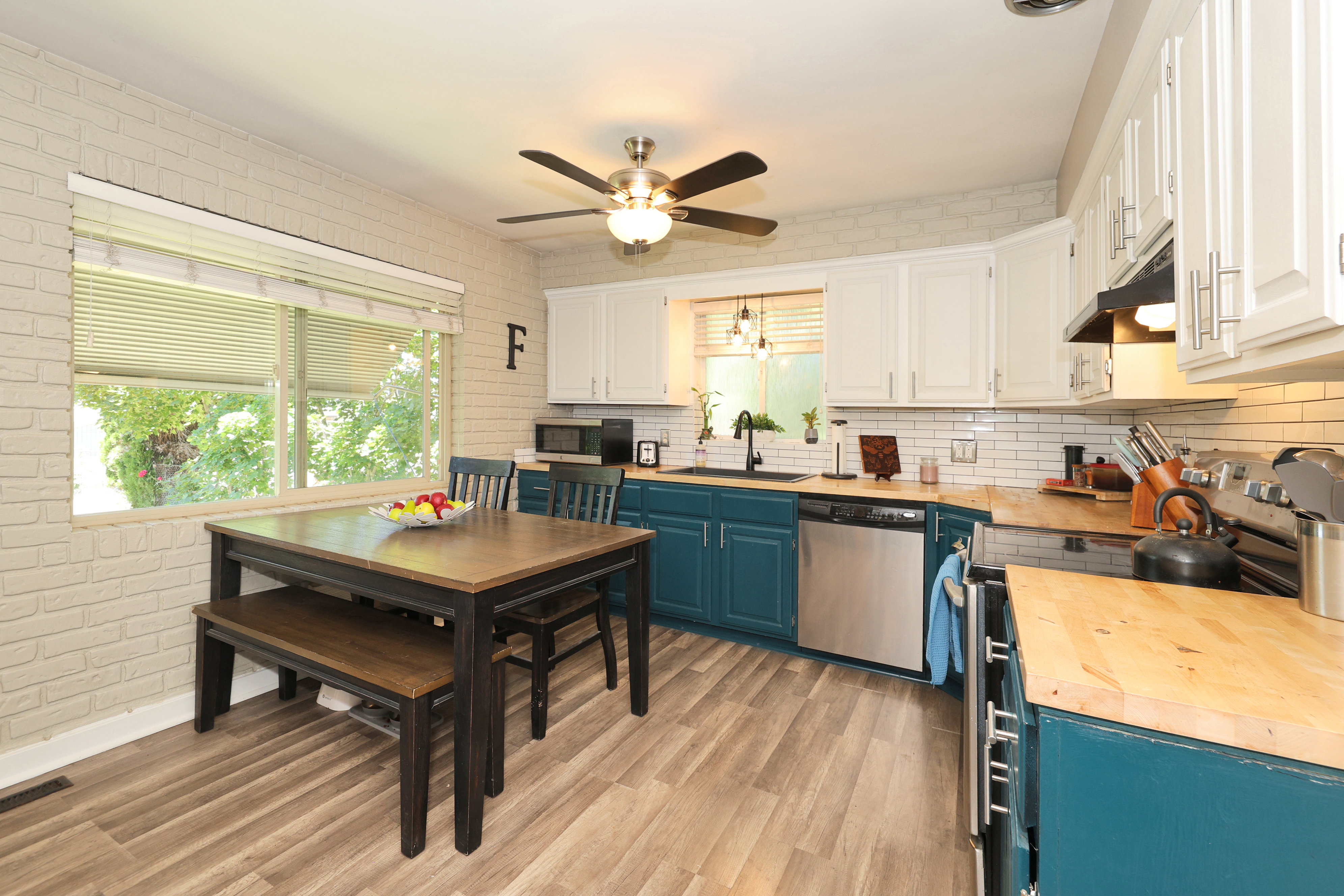 Kitchen featuring two-tone cabinetry with white upper cabinets and teal lower cabinets, wood-finish countertops, stainless steel appliances, and a subway tile backsplash