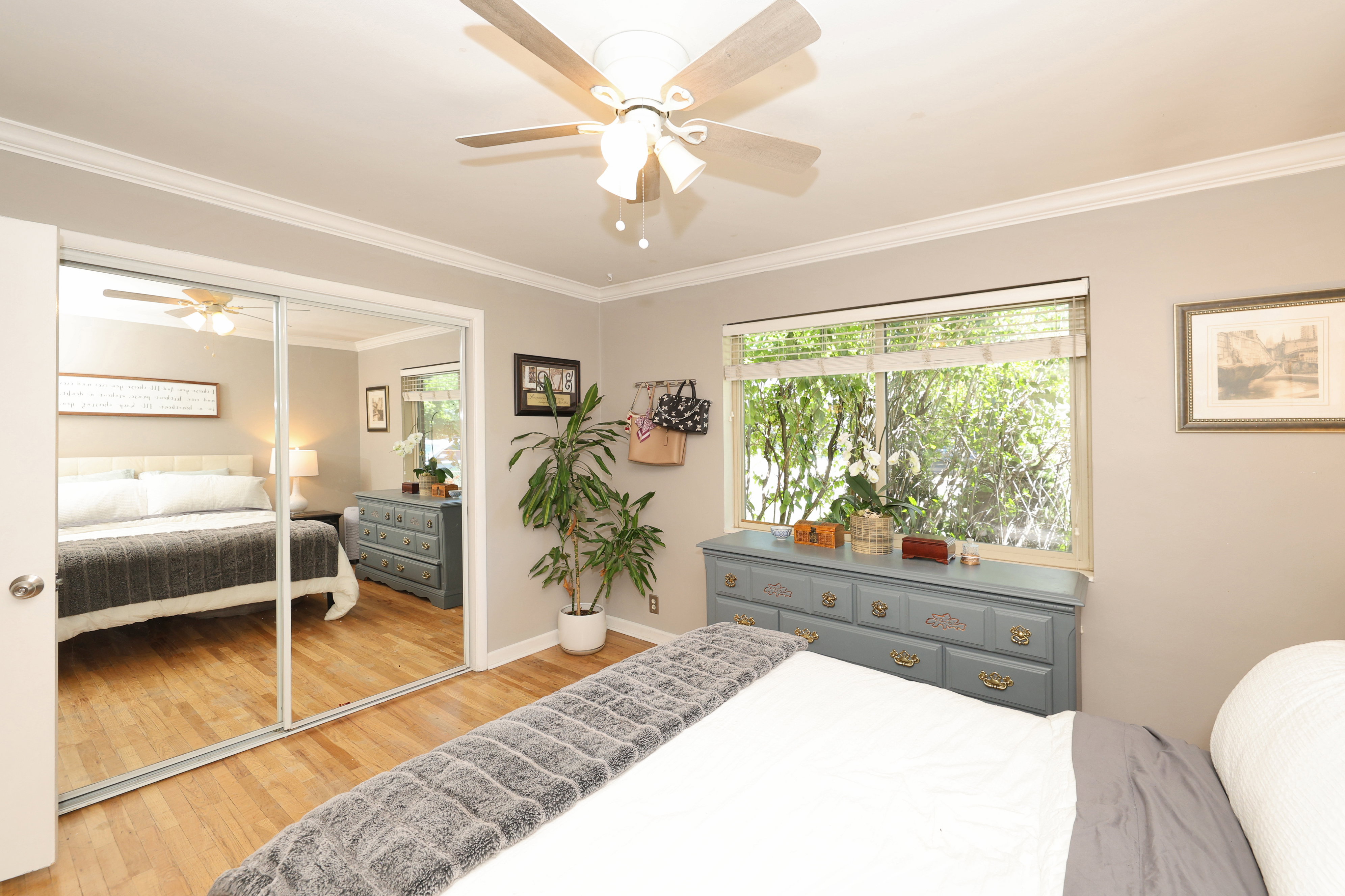 Bedroom featuring wood-finish flooring, a window with exterior tree views, crown molding, and a ceiling fan with integrated lighting