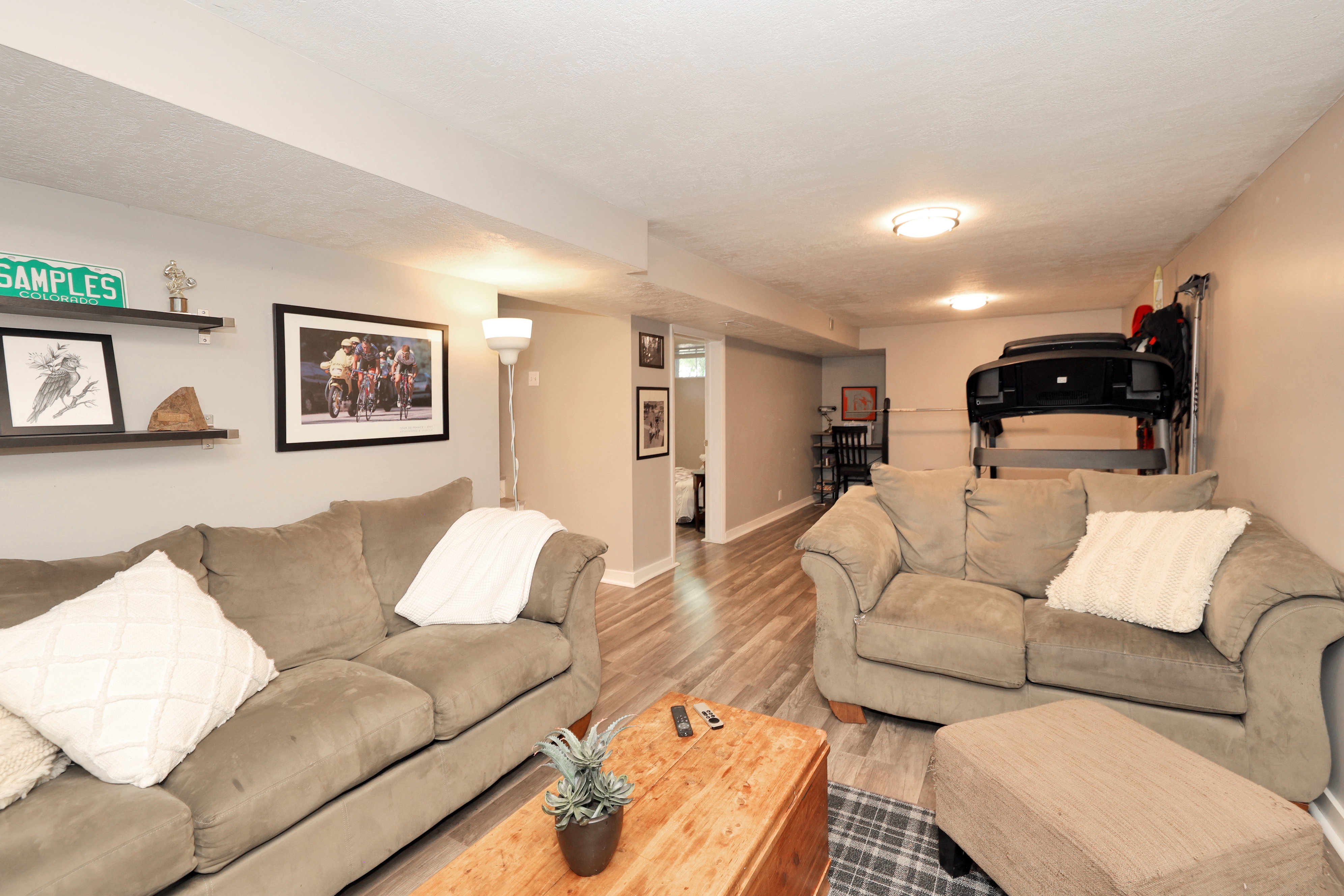 Finished lower level living space featuring light gray walls, wood-finish flooring, recessed lighting, and wall-mounted shelving