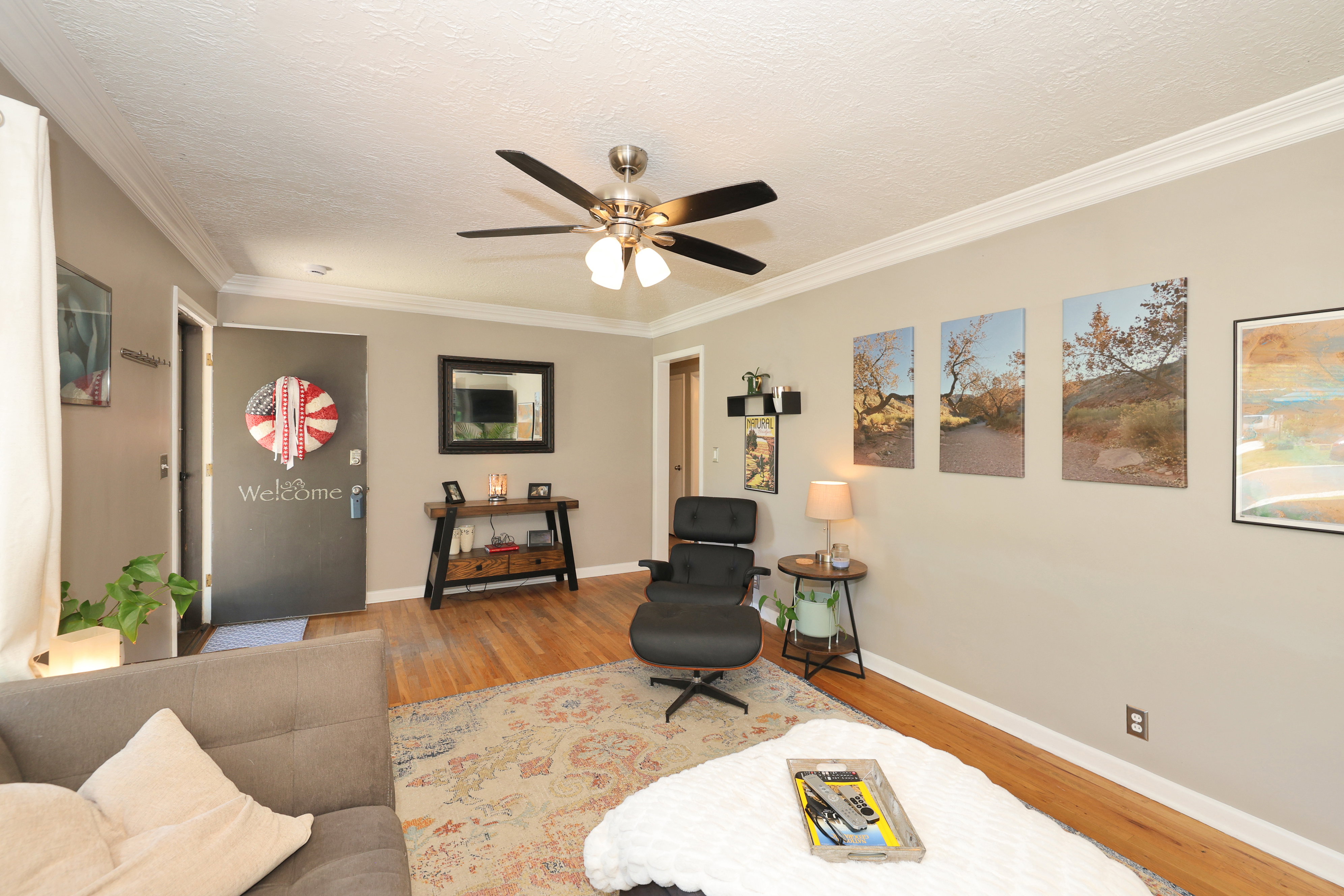 Hardwood-finish flooring, crown molding, and a ceiling fan with integrated lighting characterize this living space