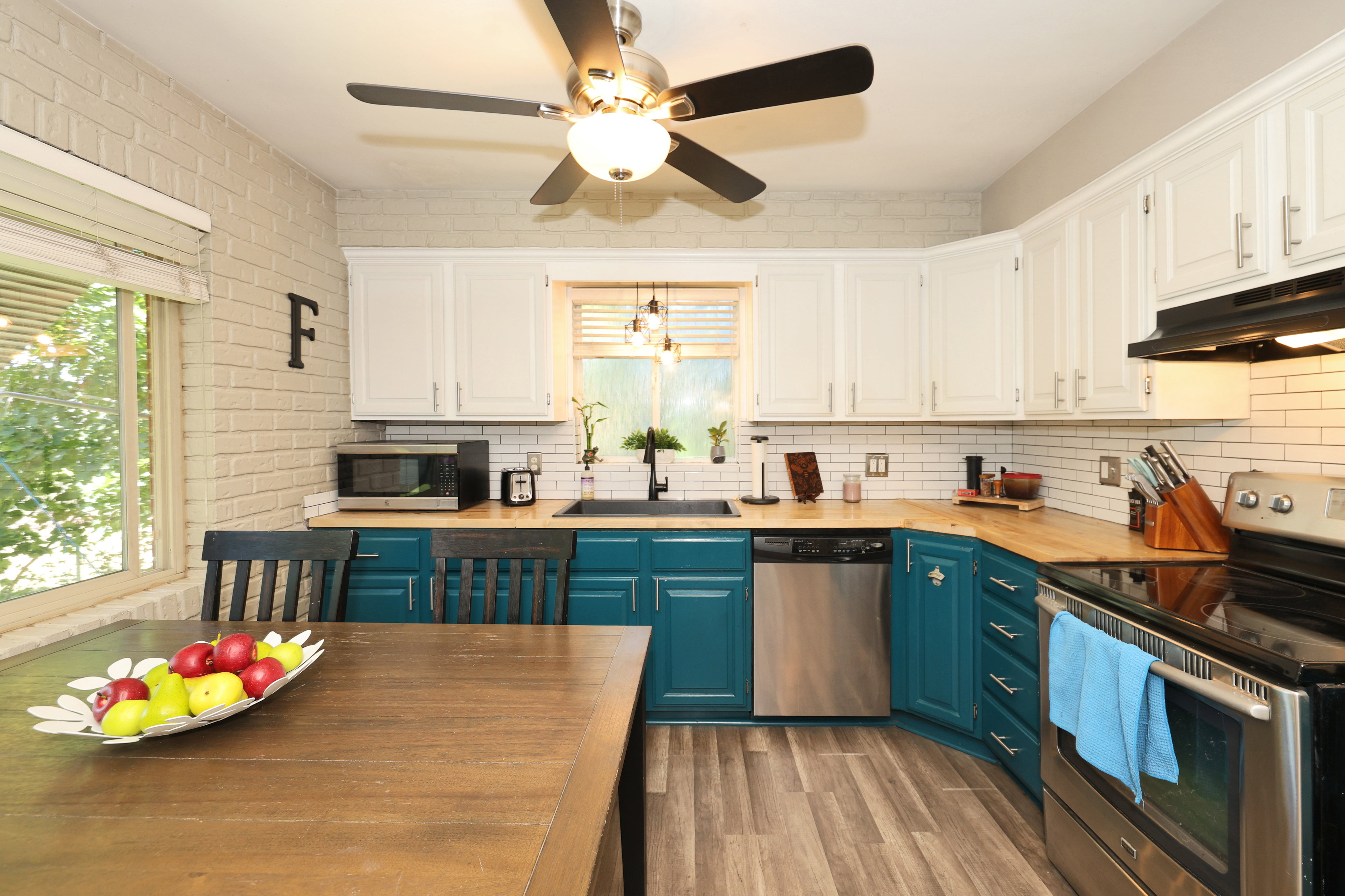 Kitchen featuring wood-finish flooring, two-tone cabinetry with white upper and teal lower cabinets, butcher block countertops, white subway tile backsplash, and stainless steel appliances