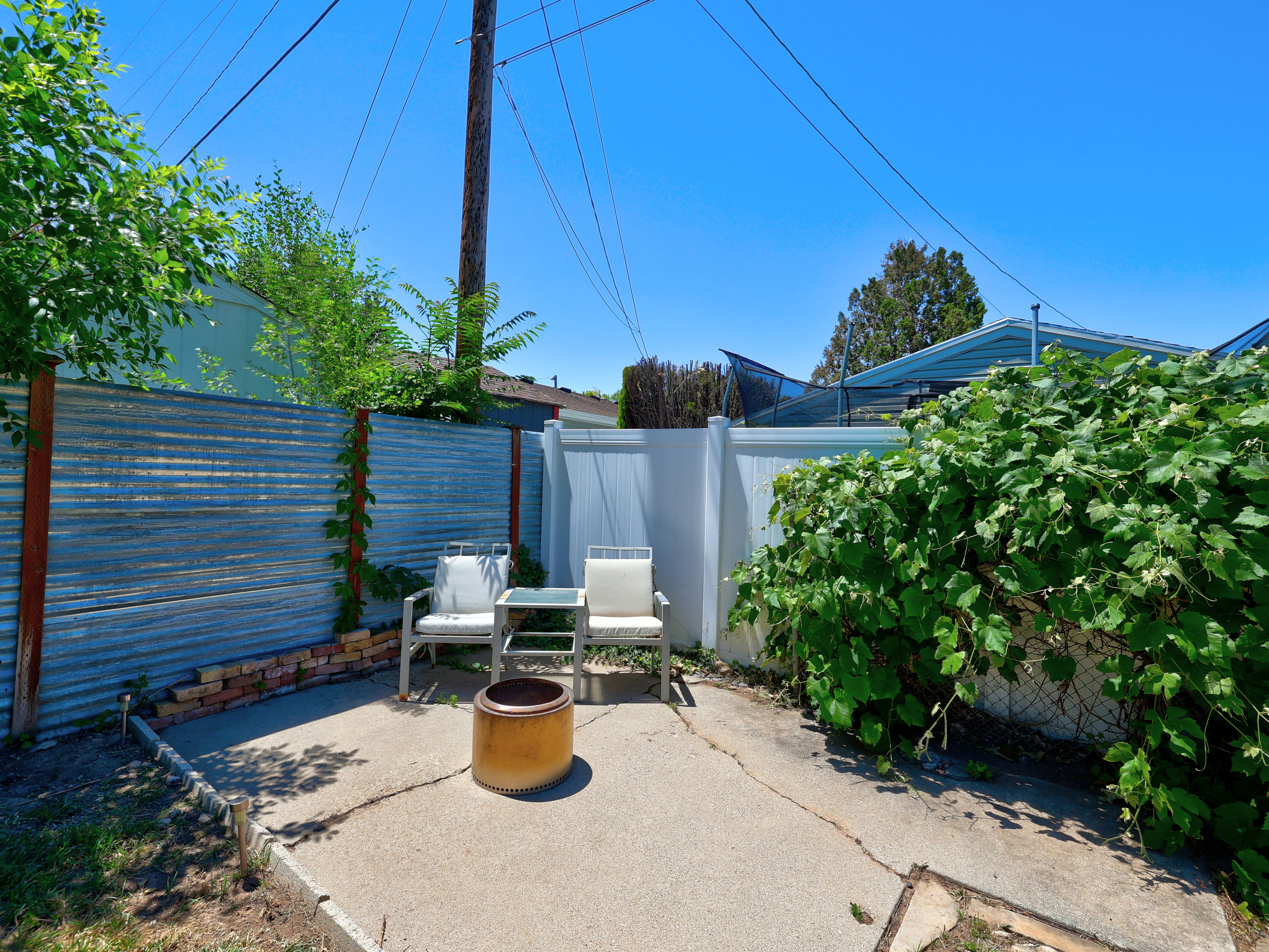 Outdoor patio area featuring a concrete pad, corrugated metal fencing, and a white privacy fence