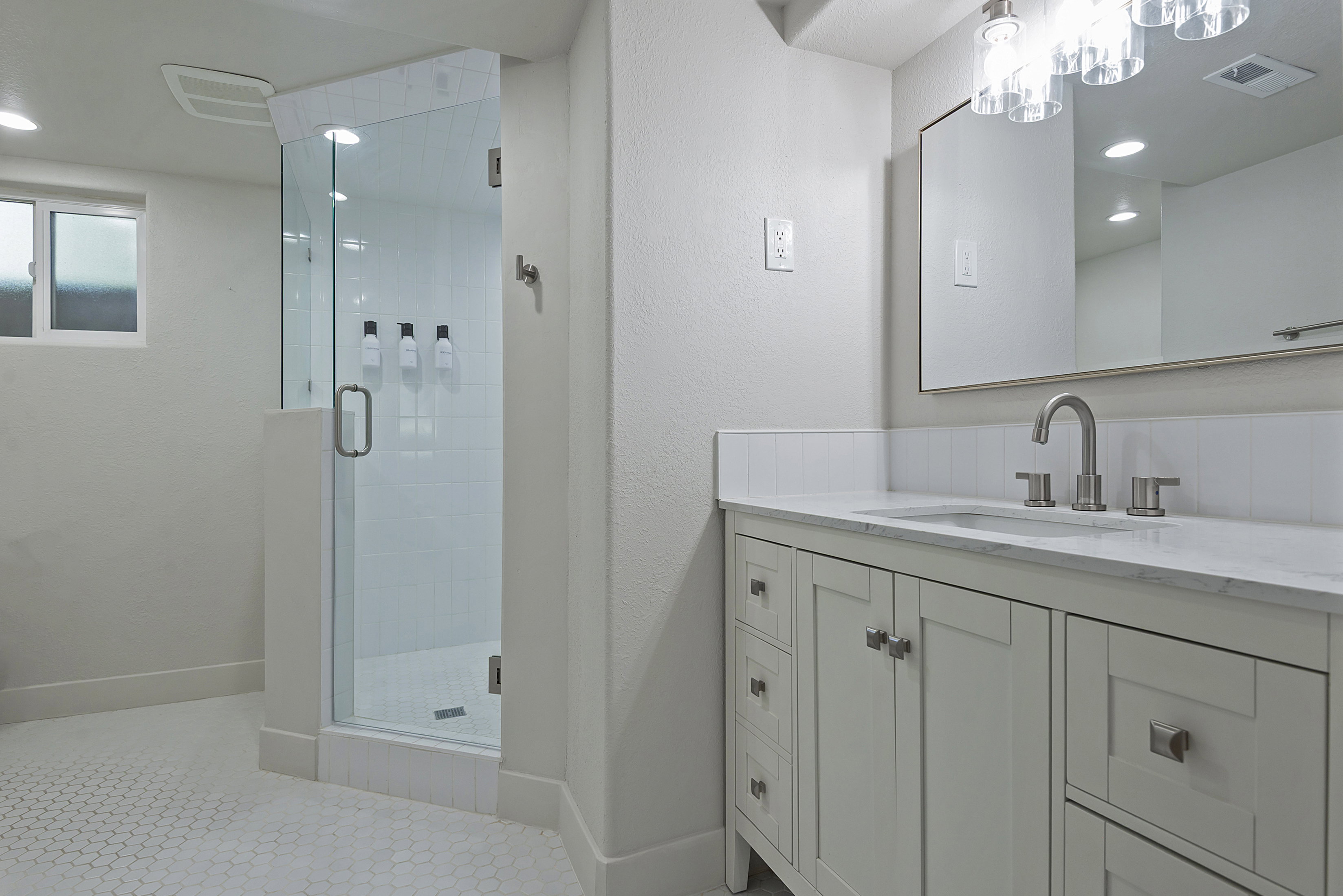 Modern bathroom featuring a glass-enclosed shower with white subway tile, a vanity with a white countertop and undermount sink, and hexagonal tile flooring