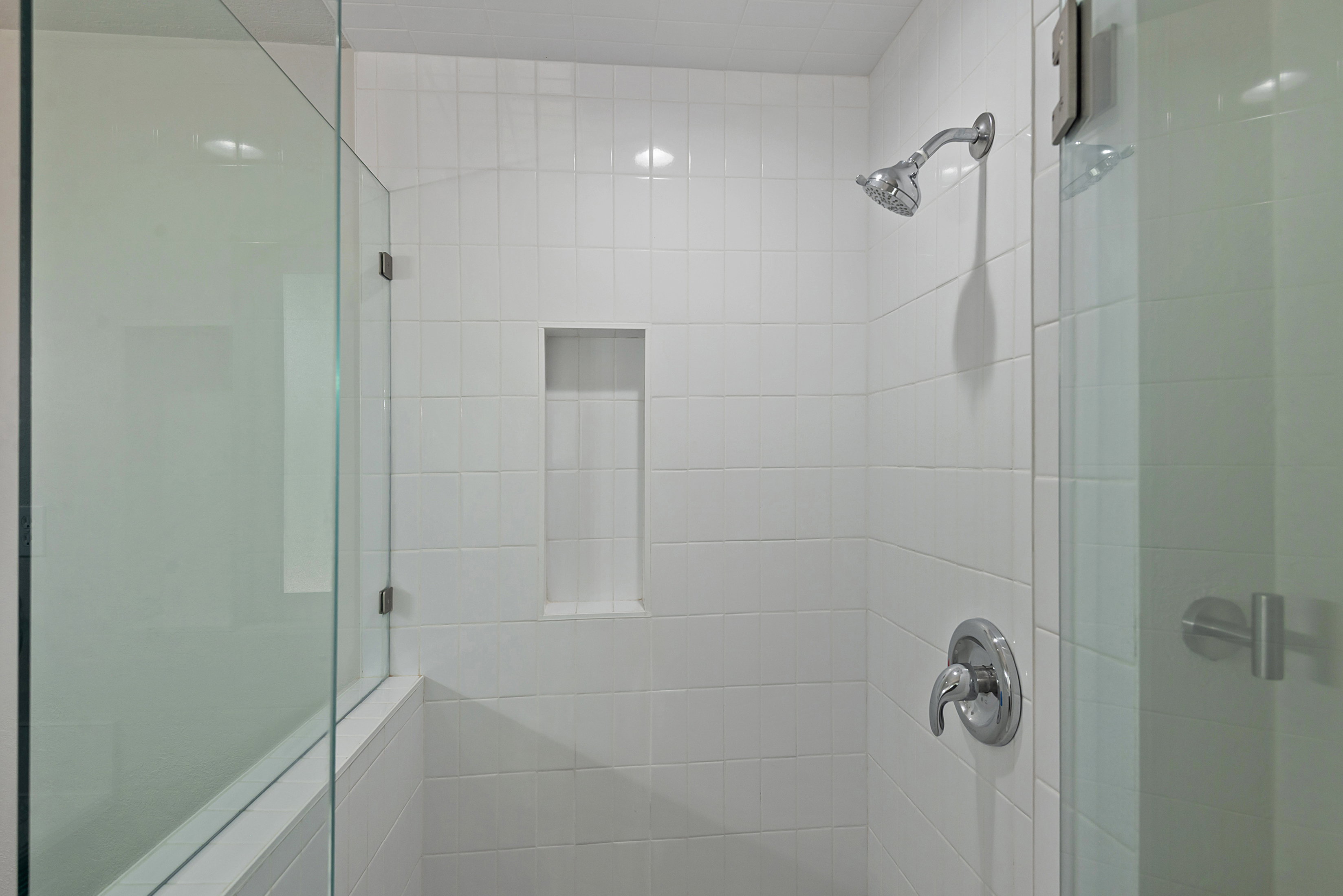 Shower enclosure featuring white subway tile, a built-in niche, and a glass partition