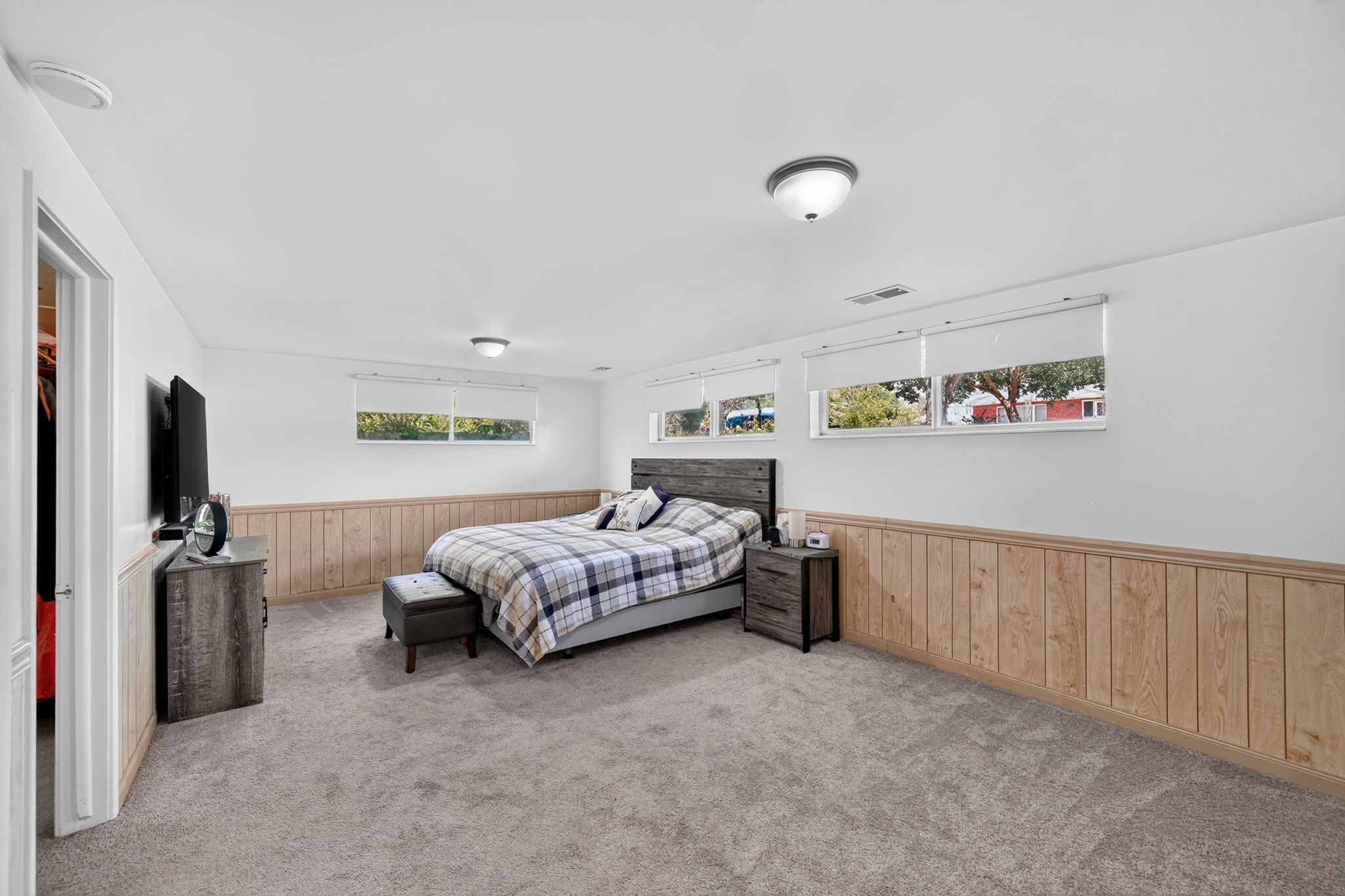 Spacious room featuring light-colored carpeting, white walls, and wood paneling along the lower wall