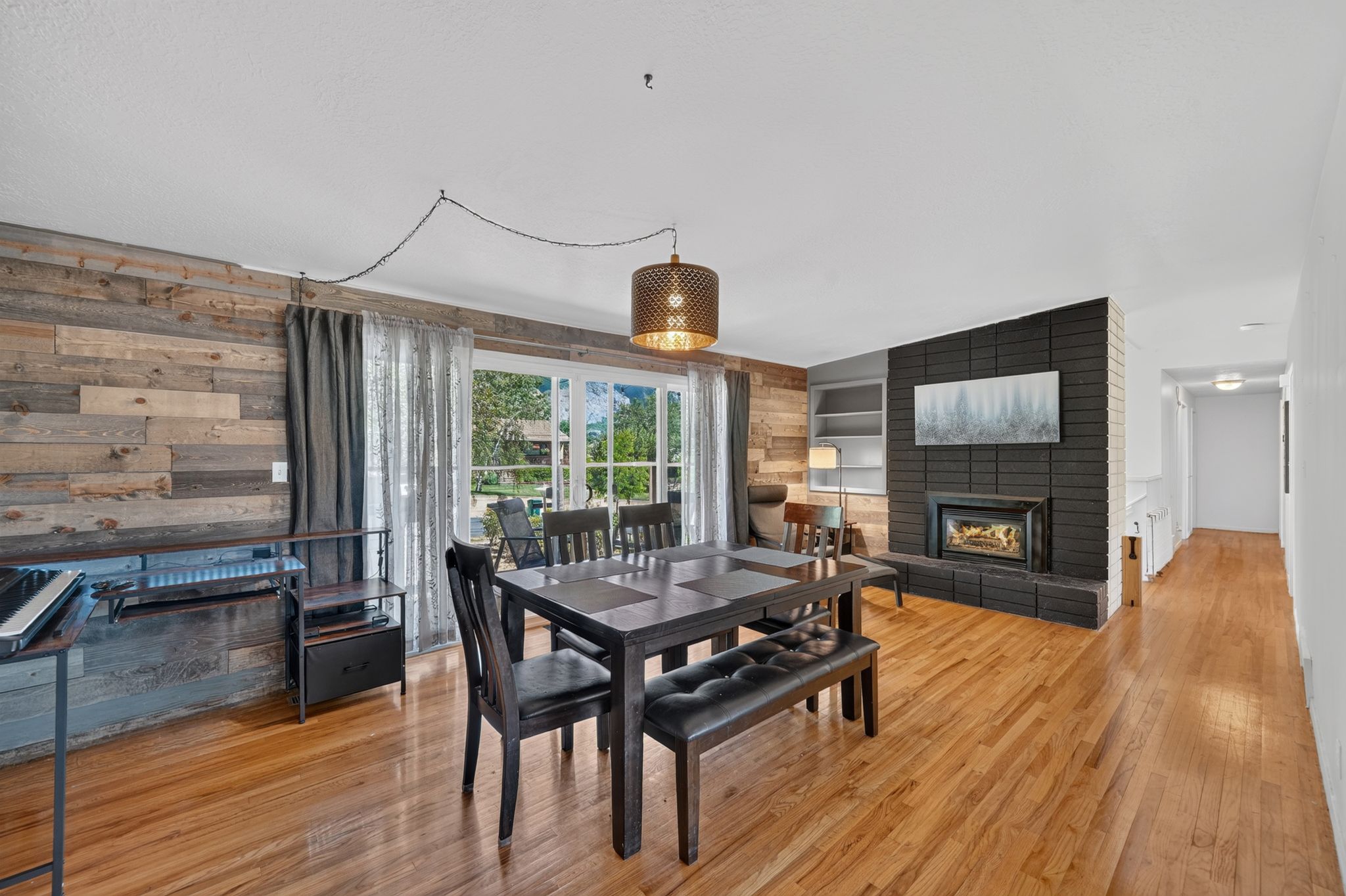 Spacious interior featuring wood-finish flooring, a prominent black brick fireplace, a feature wall with horizontal wood paneling, built-in shelving, and large sliding glass doors providing ample natural light