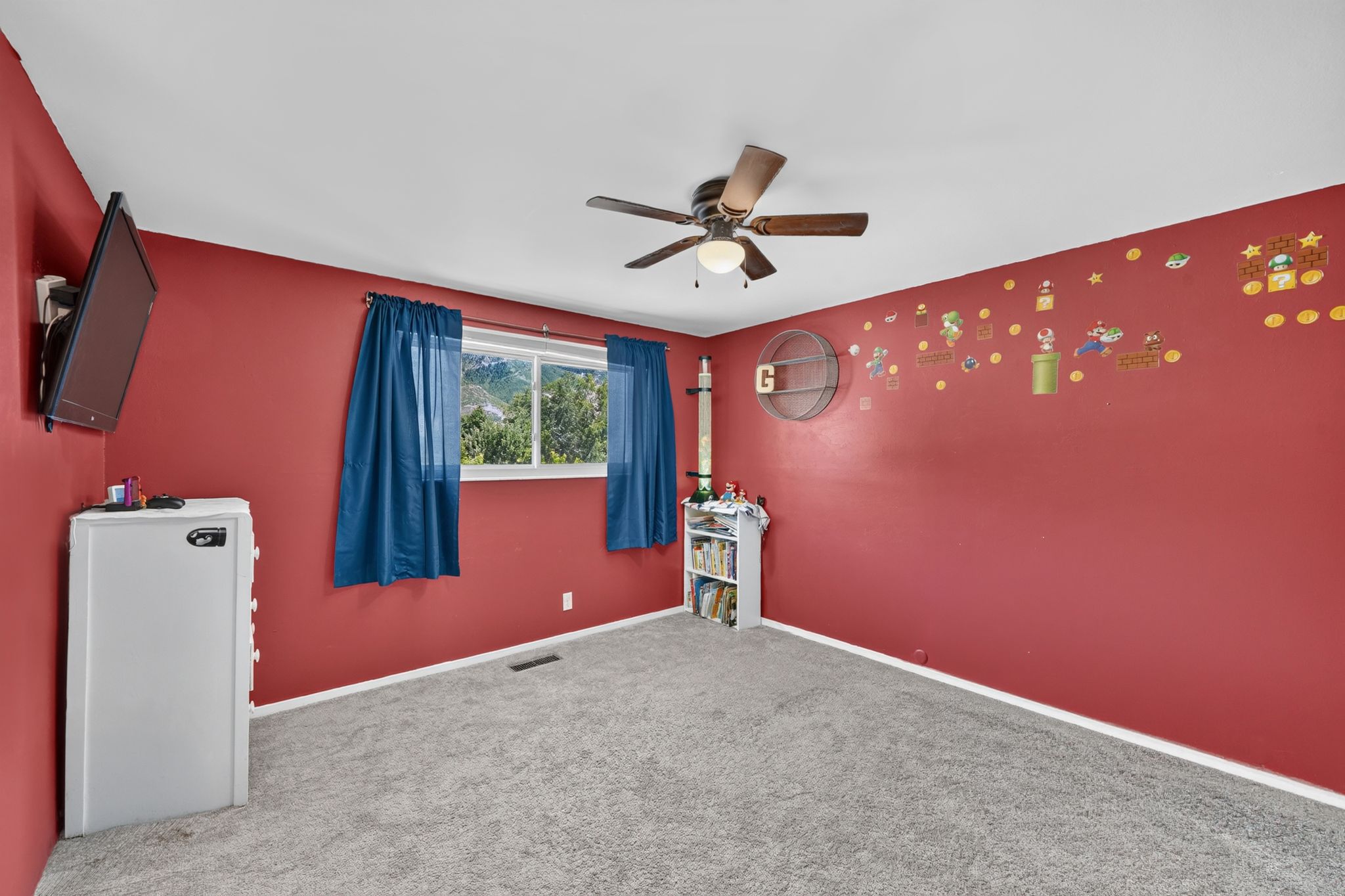 Carpeted room featuring a ceiling fan with integrated lighting, a window showcasing distant hills, and red painted walls