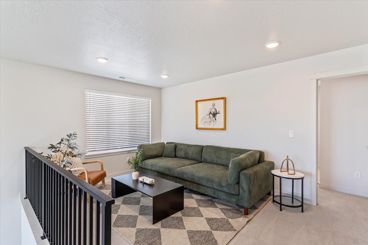 Open loft area featuring a black metal railing, recessed lighting, a large window with blinds, and neutral carpeting