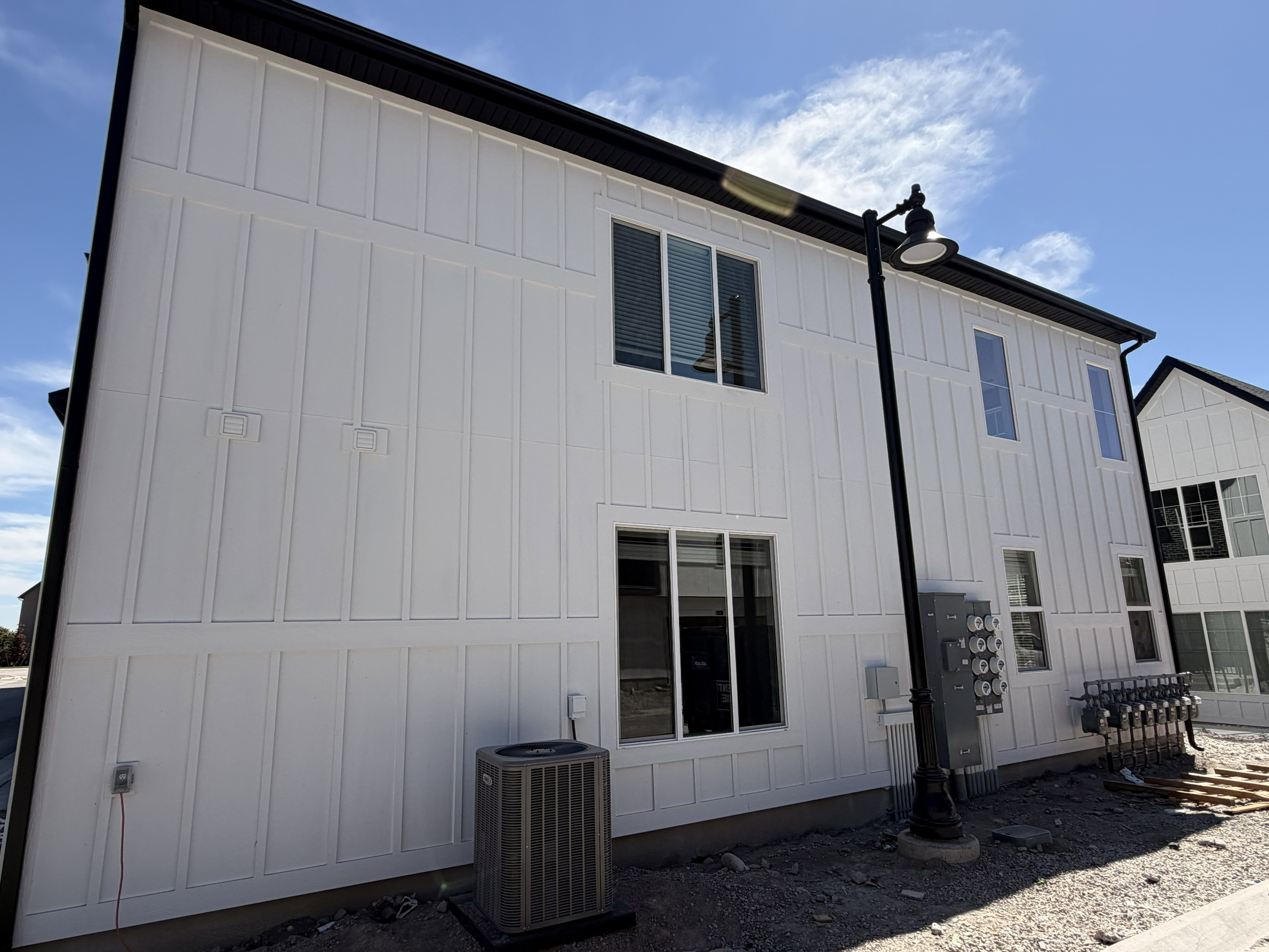 Modern white board and batten exterior with black trim, multiple windows, and a sleek black outdoor light fixture