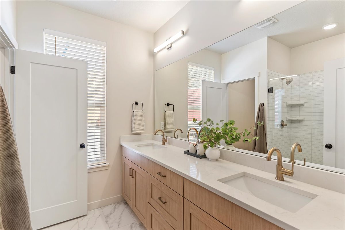 Spacious bathroom featuring a double vanity with light wood-finish cabinetry, white countertops, and dual undermount sinks with brass-tone fixtures