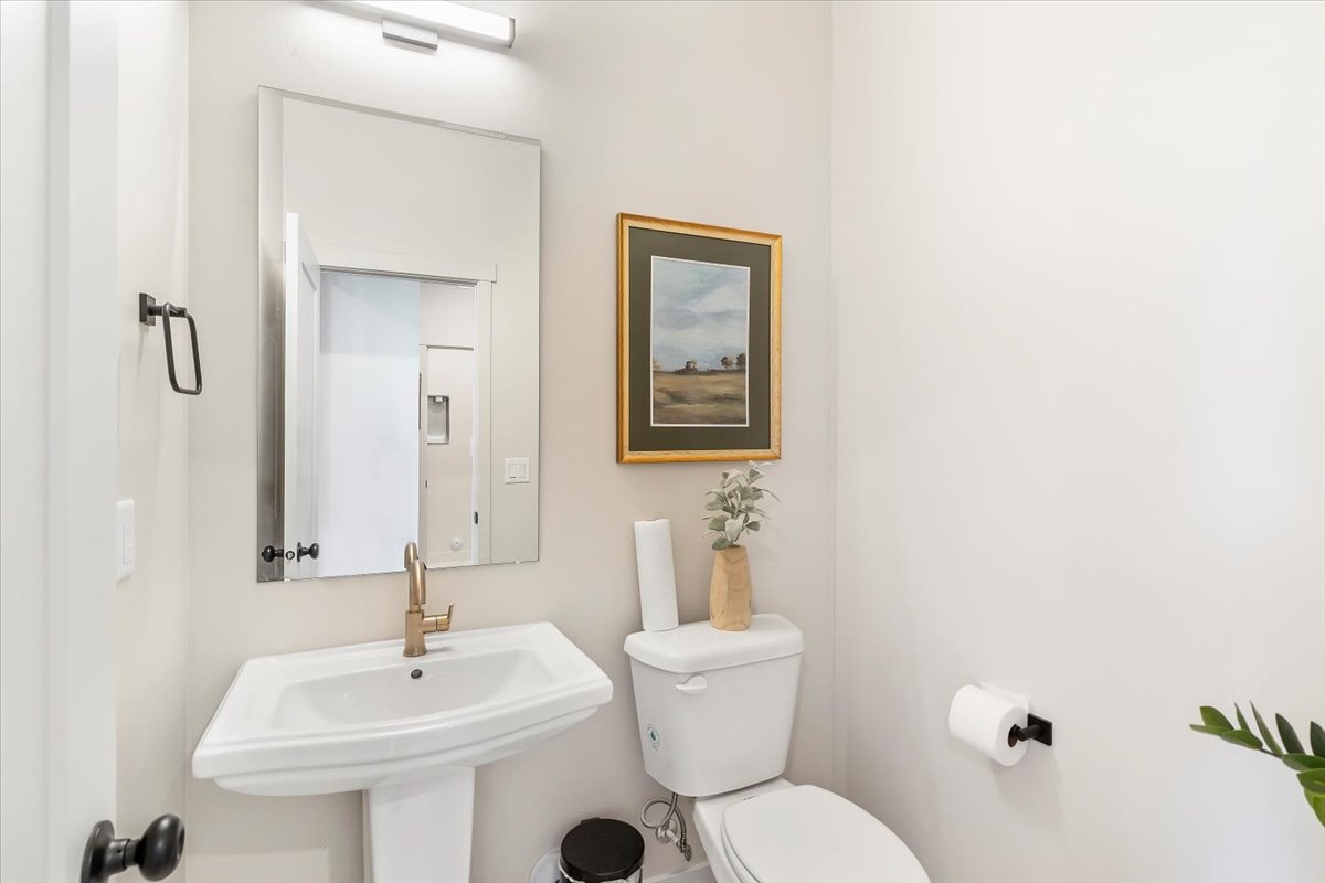 Pedestal sink with a gold-tone faucet, complemented by a rectangular mirror and overhead vanity lighting