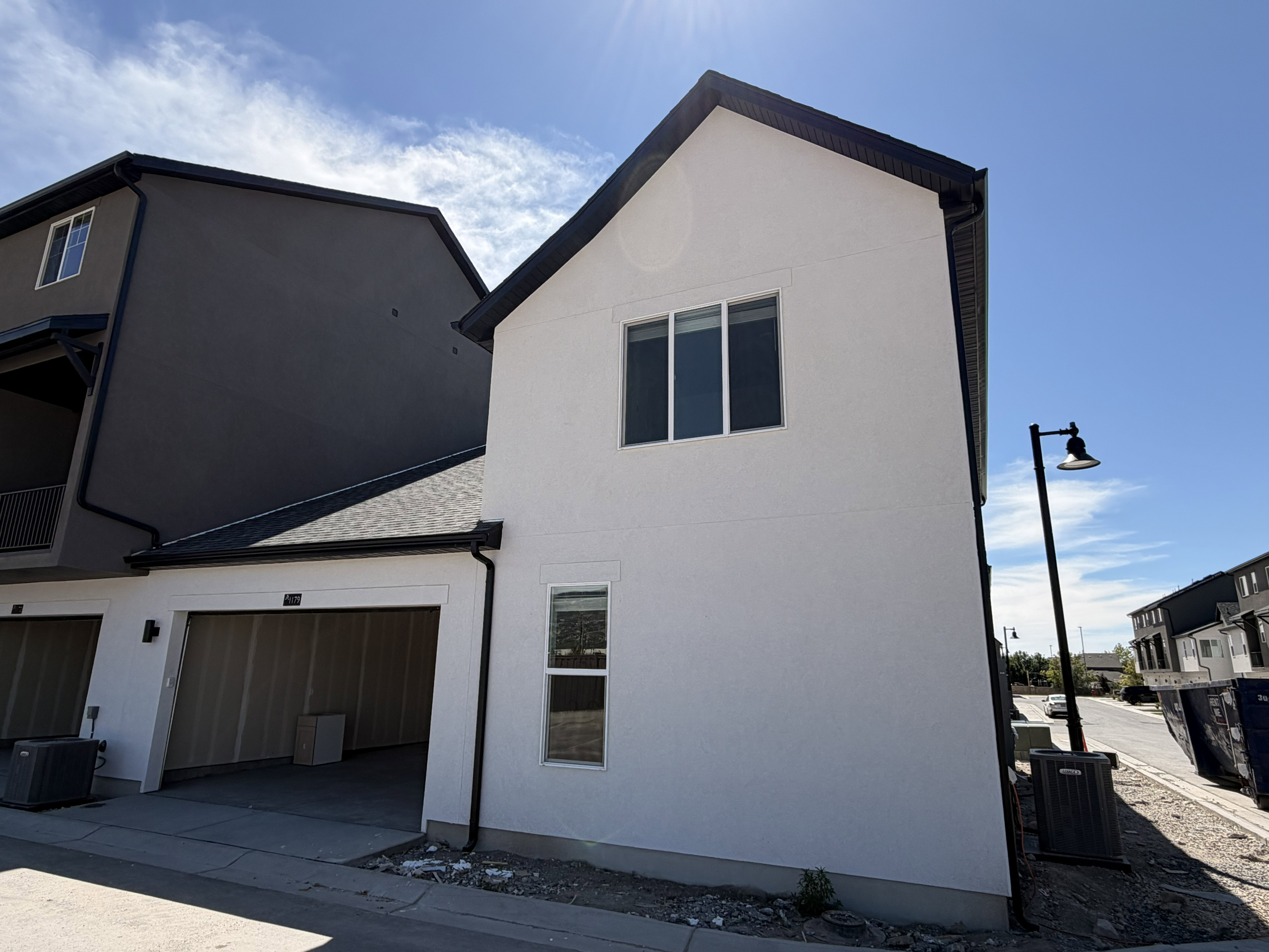 White stucco exterior with a dark-pitched roof, featuring a two-car garage with a light wood-finish door
