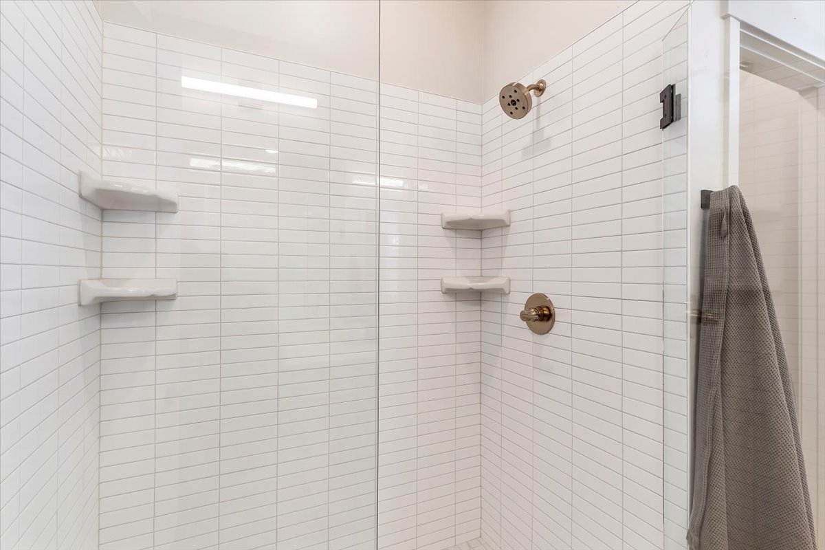 Shower enclosure featuring clear glass panels, white subway tile, a bronze shower head, a bronze control valve, and two built-in corner shelves