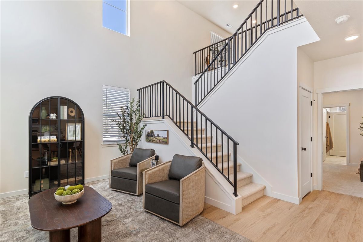 Two-story entry featuring light wood-finish flooring, a carpeted staircase with black metal railings, and a high ceiling with an upper-level window