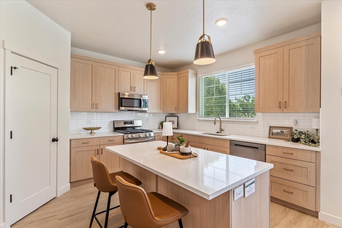 Modern kitchen featuring a central island with a solid surface countertop, light wood-finish cabinetry, stainless steel appliances, a tile backsplash, and recessed lighting