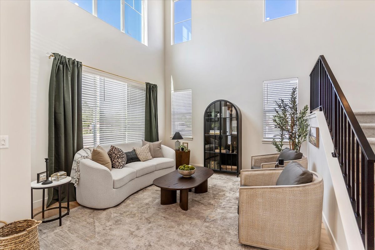 Vaulted ceilings with high windows, wood-finish flooring, a contemporary staircase with iron railings, and multiple windows with blinds