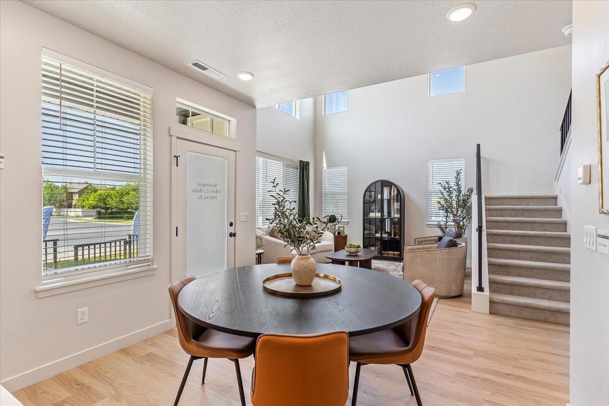 Open-concept dining and living area featuring high ceilings, wood-finish flooring, recessed lighting, and a carpeted staircase with a dark handrail