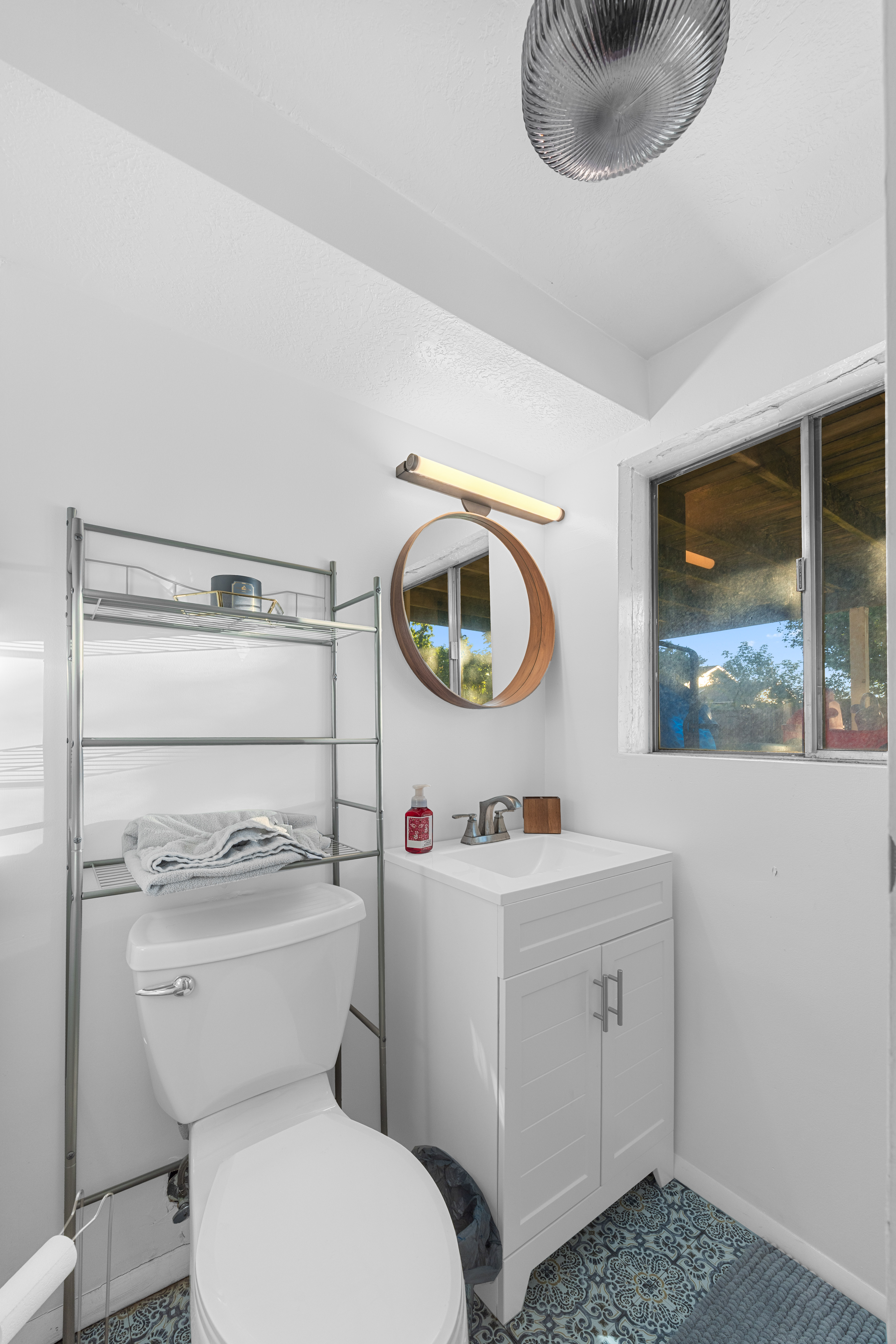 Compact bathroom featuring a white toilet, white vanity with cabinet storage, and a circular mirror