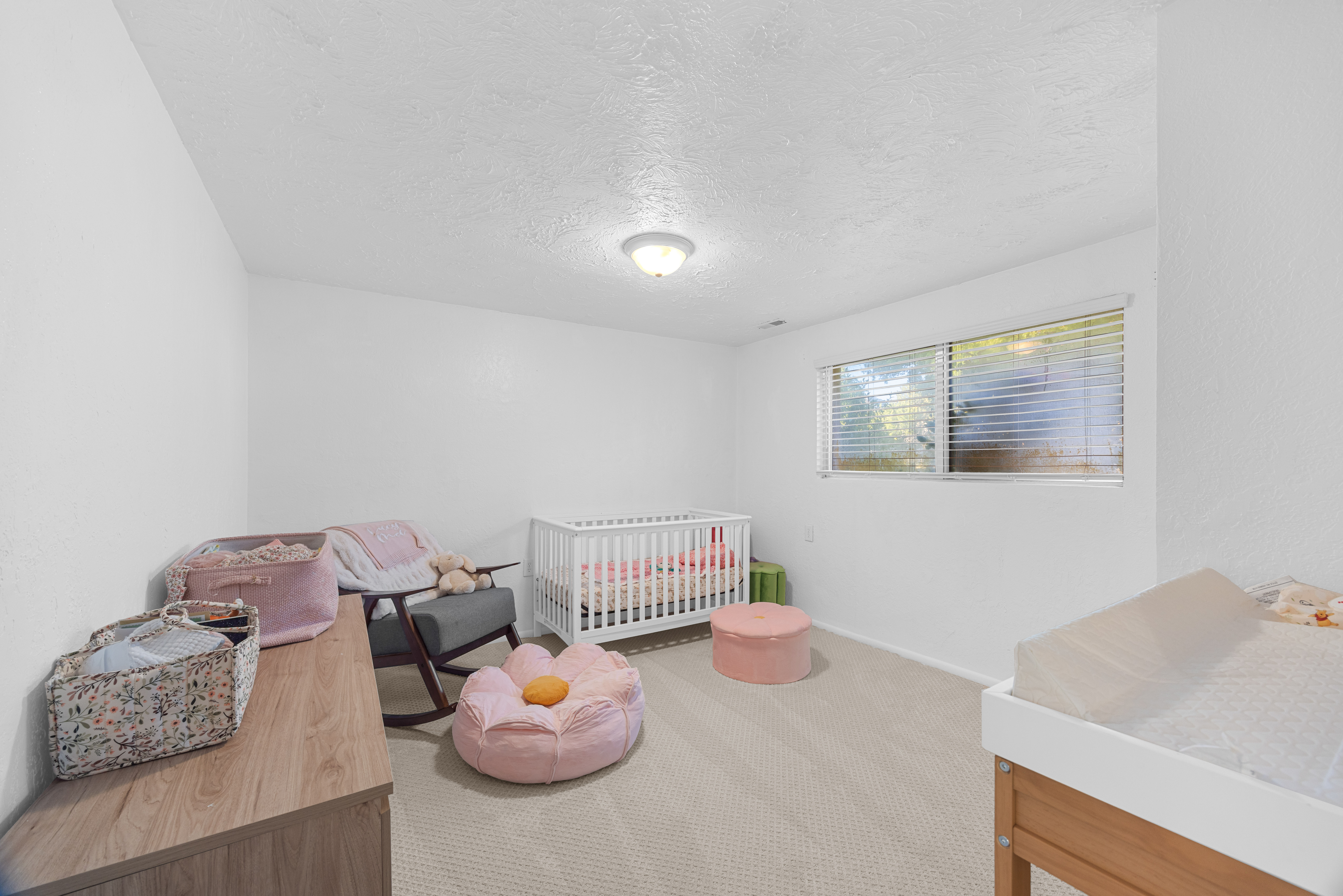 Neutral toned carpeting, a window with horizontal blinds, and a white ceiling with a flush-mount light fixture