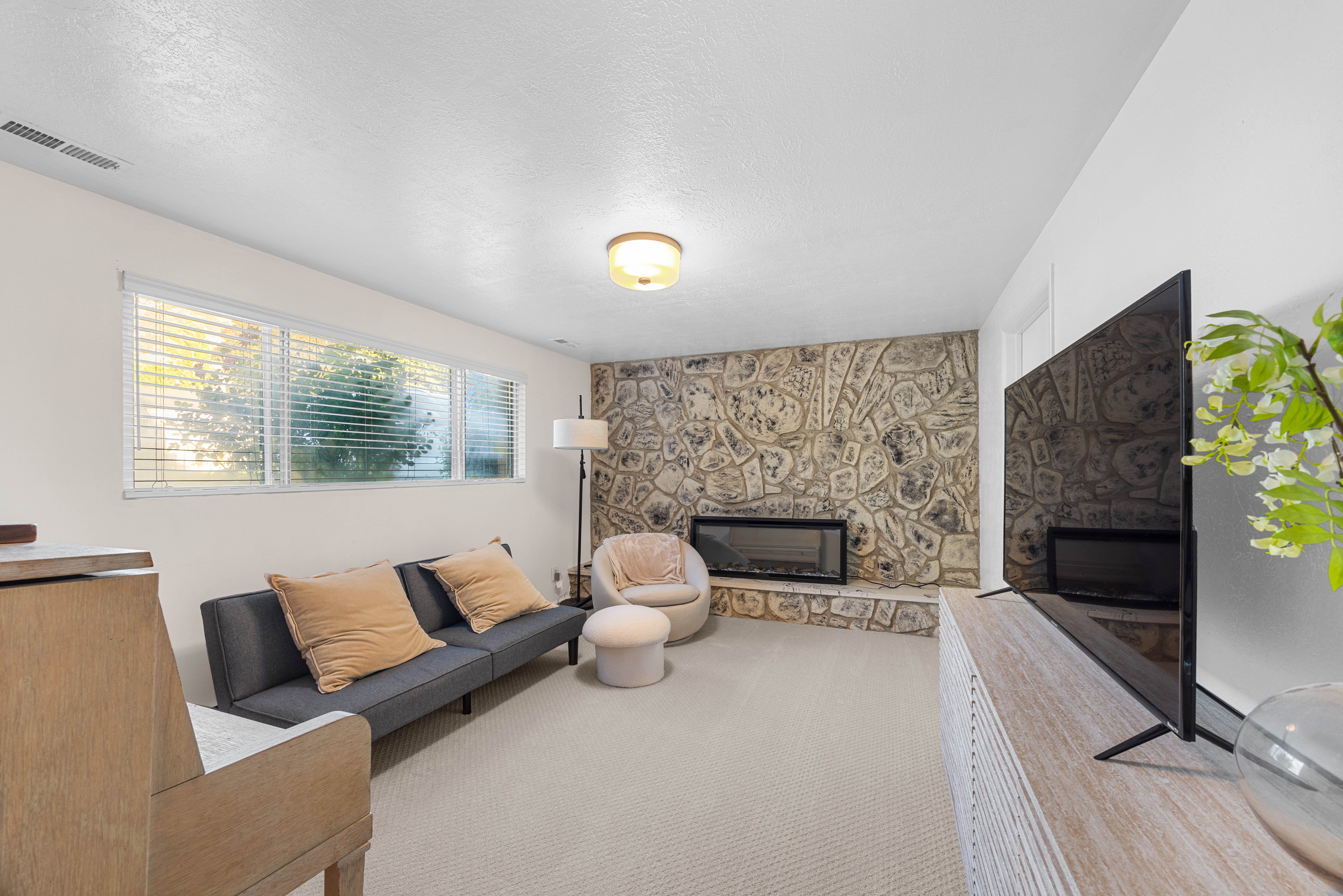 Living area featuring a stone accent wall with an inset fireplace, wall-to-wall carpeting, and a series of windows with blinds