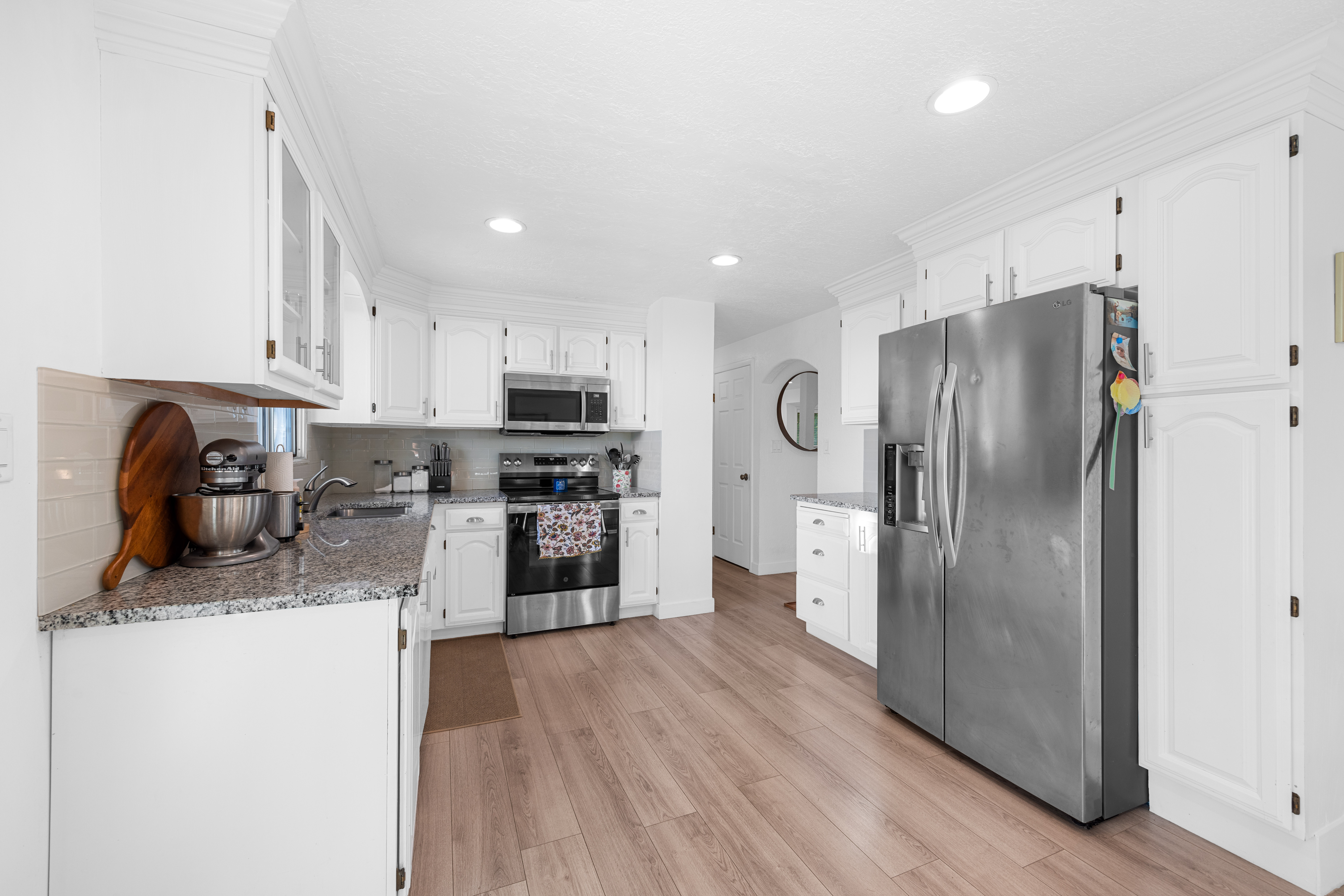 Kitchen featuring white cabinetry, granite countertops, stainless steel appliances, wood-finish flooring, and recessed lighting