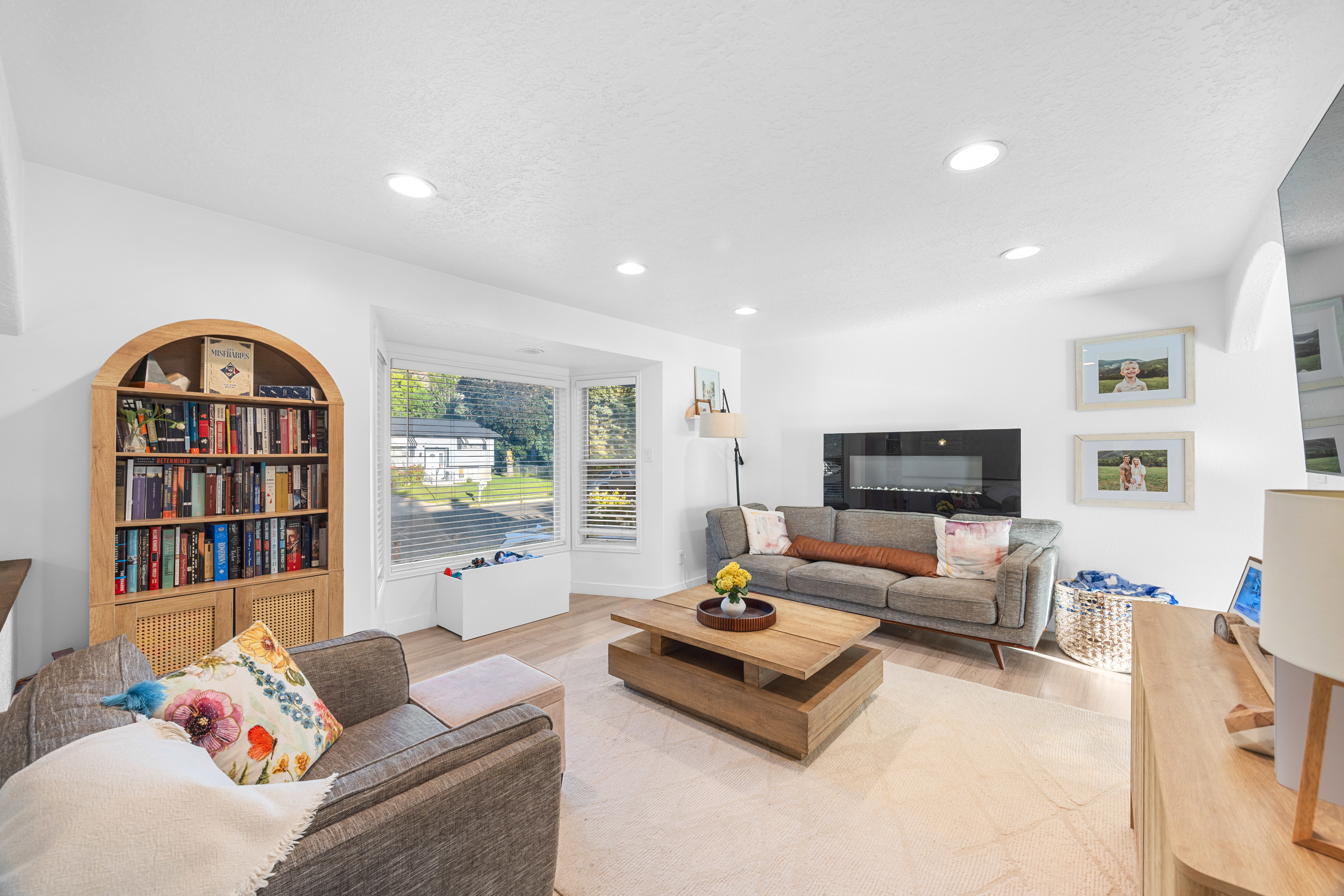 Bright living area featuring wood-finish flooring, recessed lighting, a modern wall-mounted fireplace, and a bay window