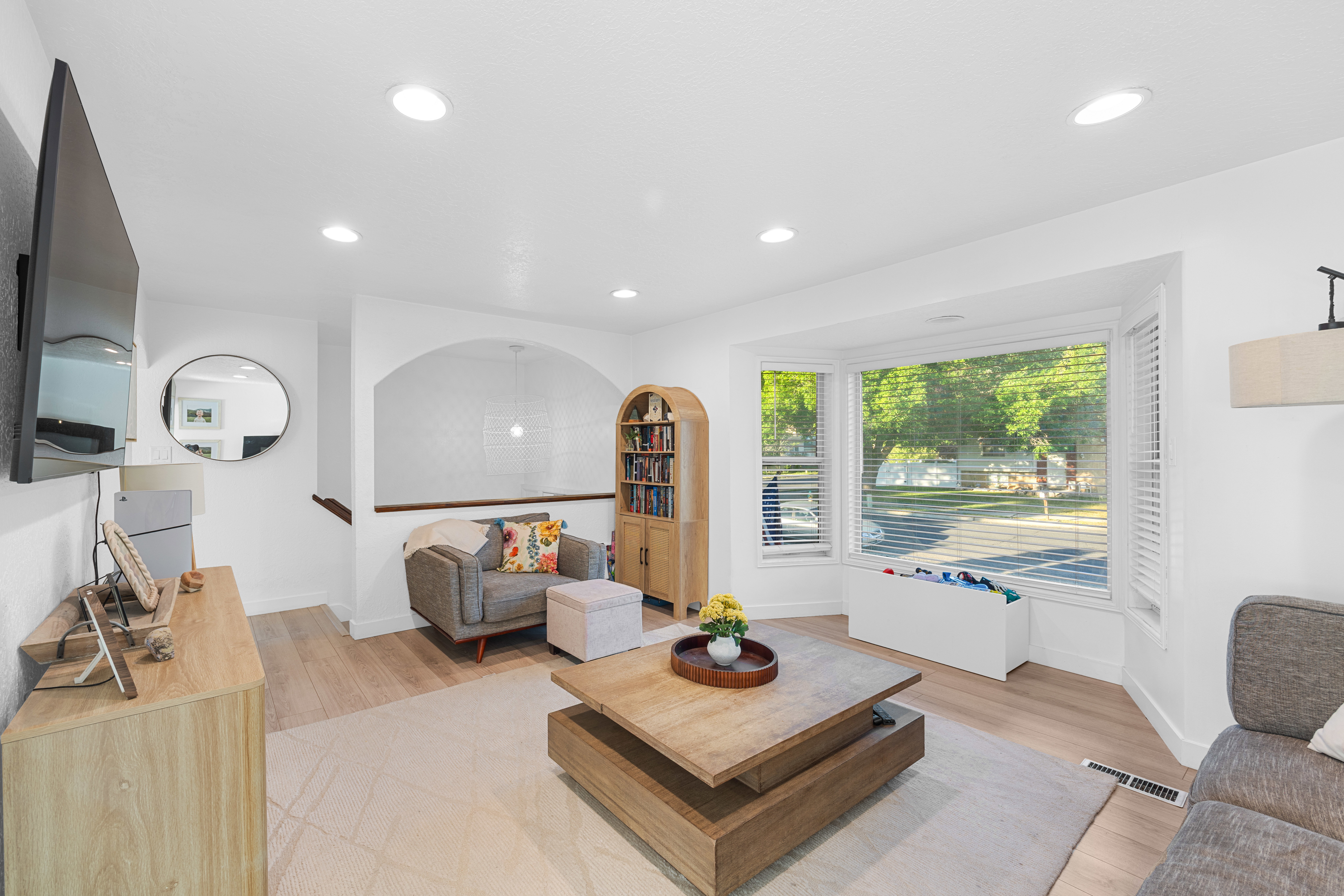 Living area featuring light wood-finish flooring, recessed lighting, and a bay window with plantation shutters