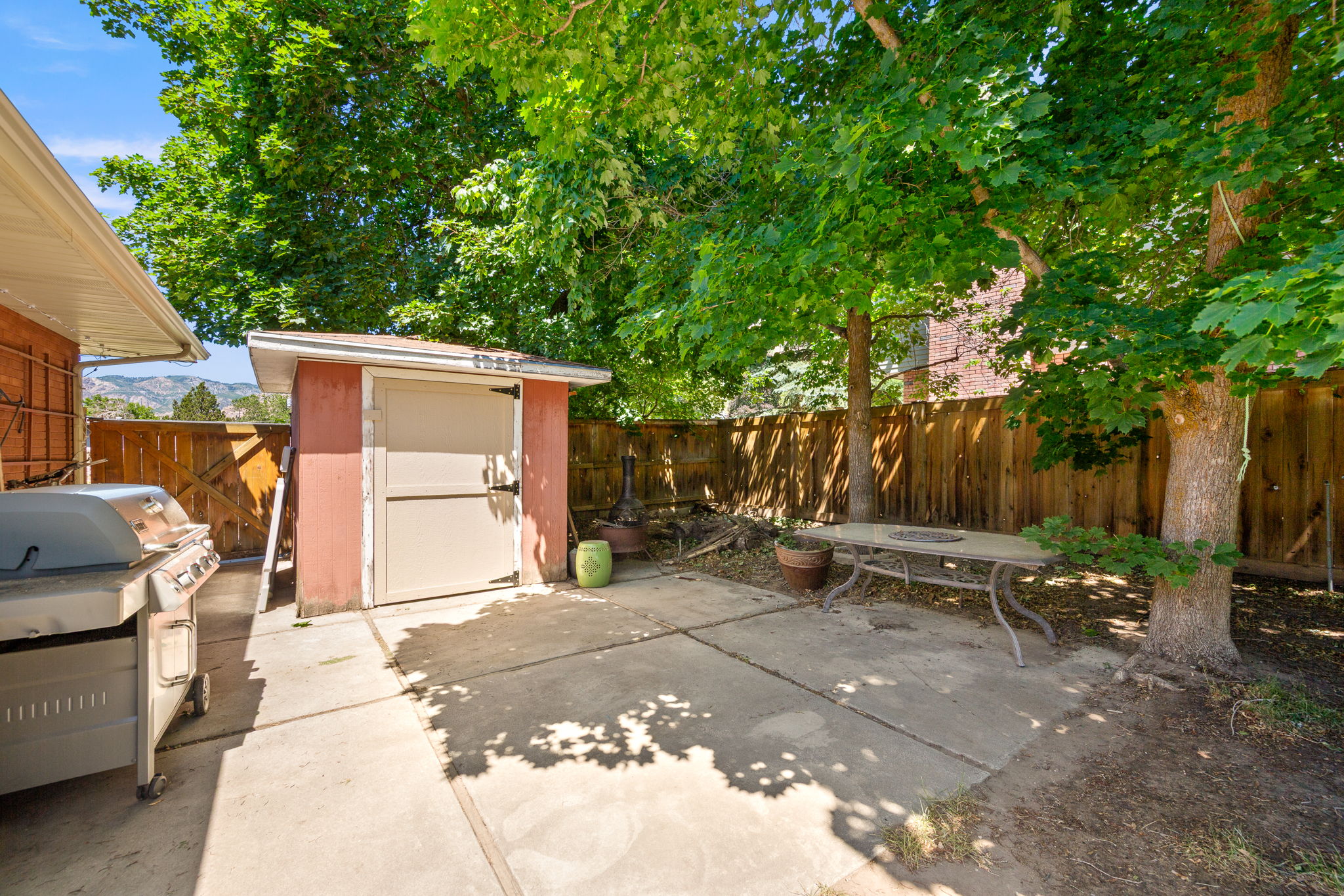 Outdoor patio space with a built-in storage shed, concrete paving, a wood fence perimeter, and mature trees providing natural canopy!