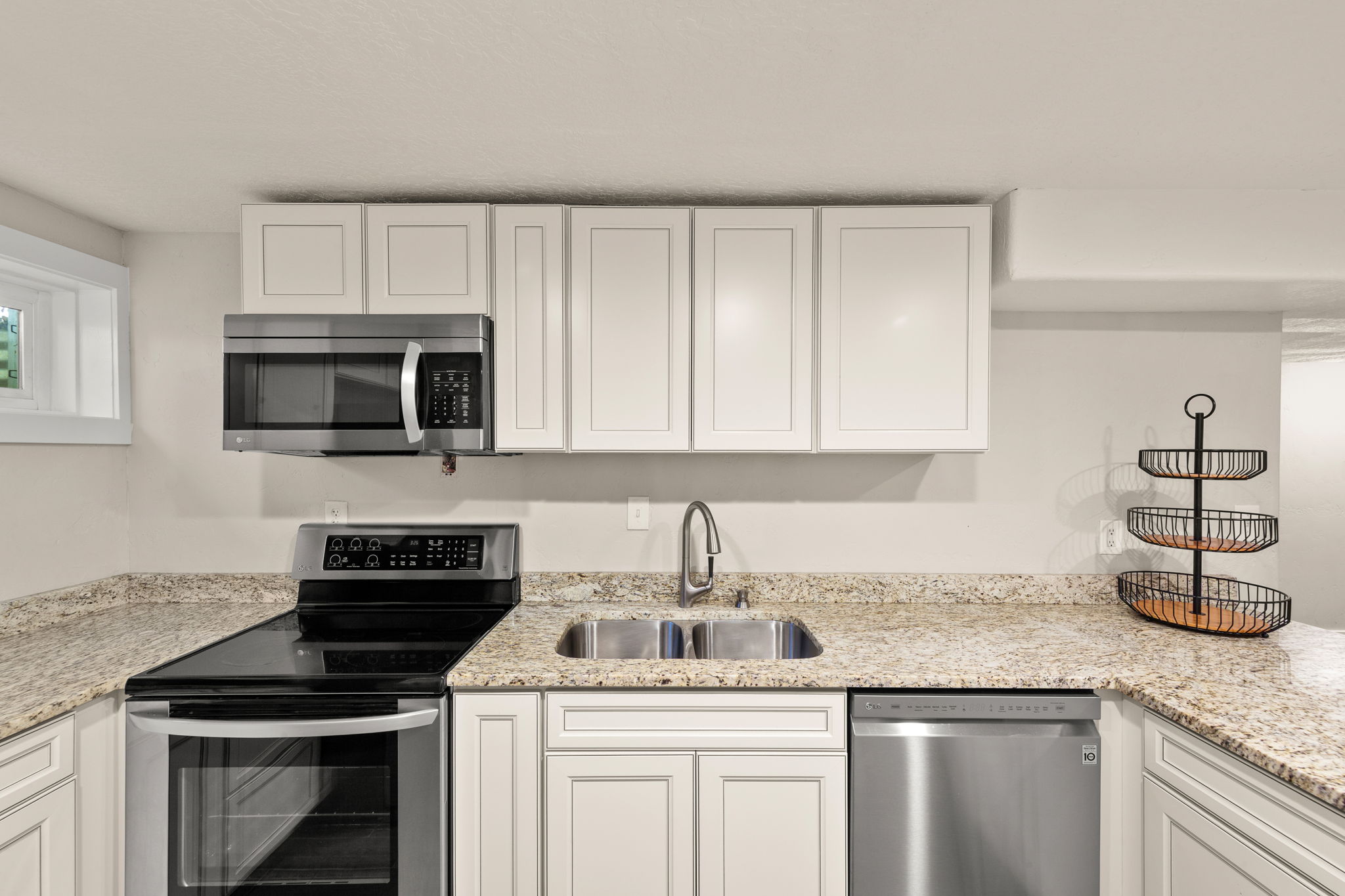 Modern kitchen featuring white shaker cabinetry, stainless steel appliances, speckled stone countertops, and a double basin sink with a gooseneck faucet!  Lots of Counter Space!