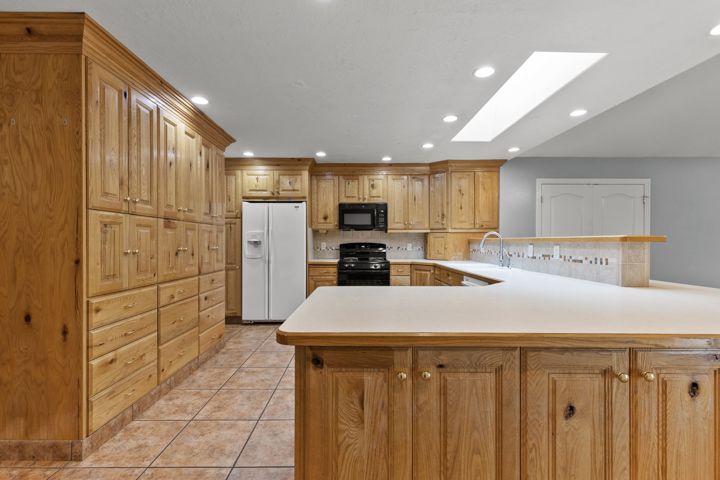 Kitchen featuring wood cabinetry, integrated appliances, recessed lighting, and a skylight