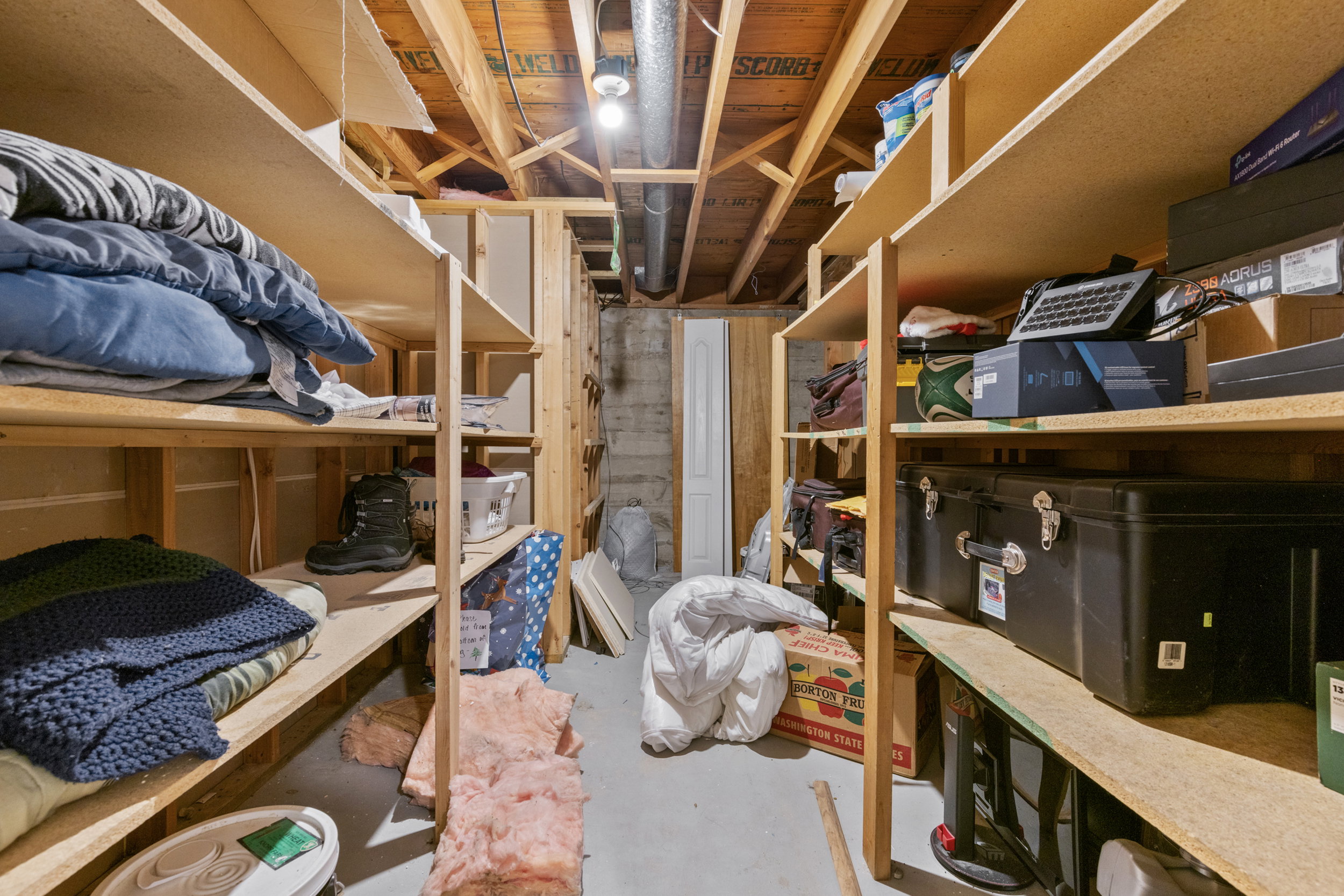 Expansive storage room featuring built-in shelving, concrete flooring, exposed ceiling joists, overhead lighting, and visible ductwork