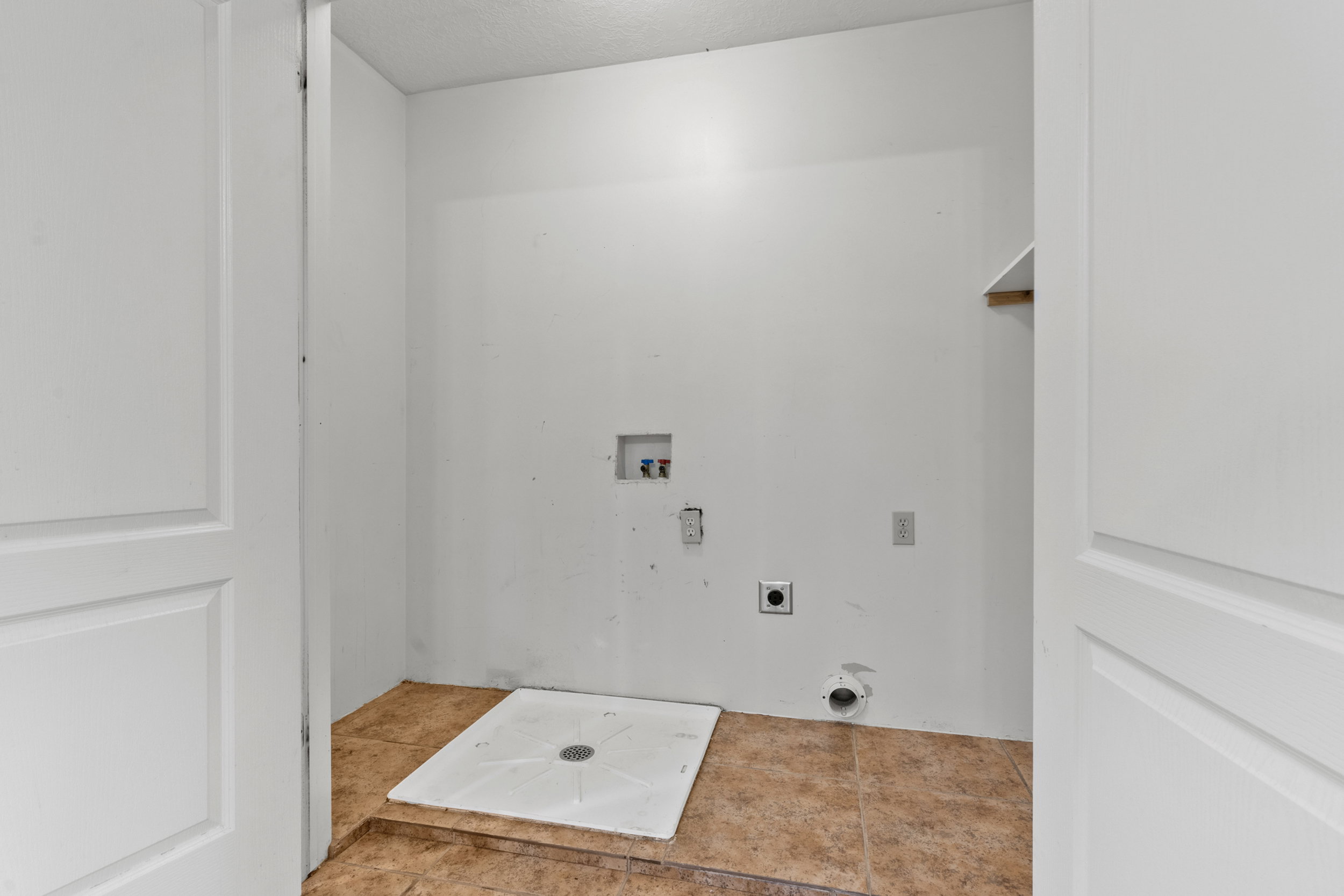 Utility room featuring ceramic tile flooring, white walls, and a built-in shelf