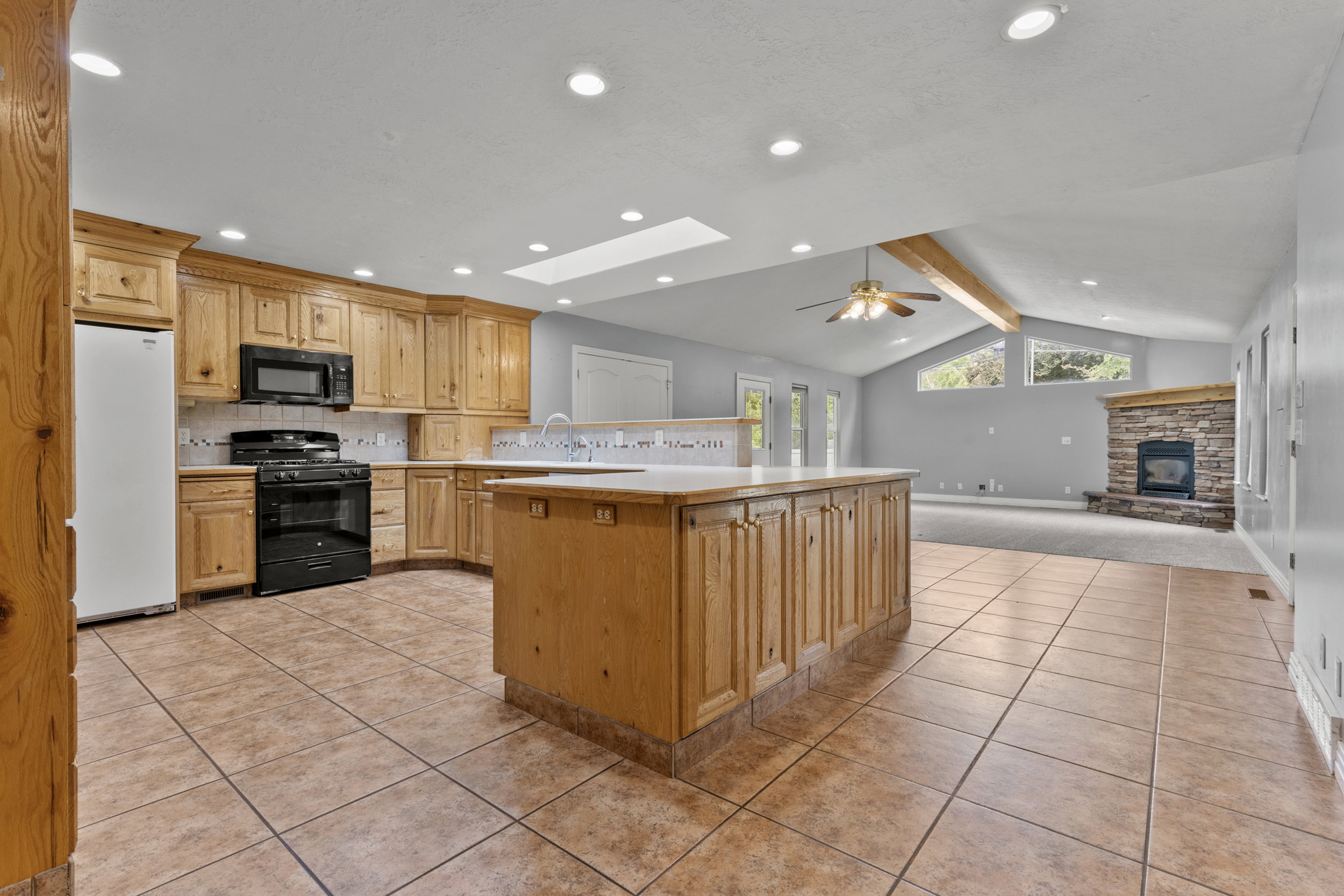Open-concept kitchen and living area featuring a central island, wood cabinetry, recessed lighting, and tile flooring